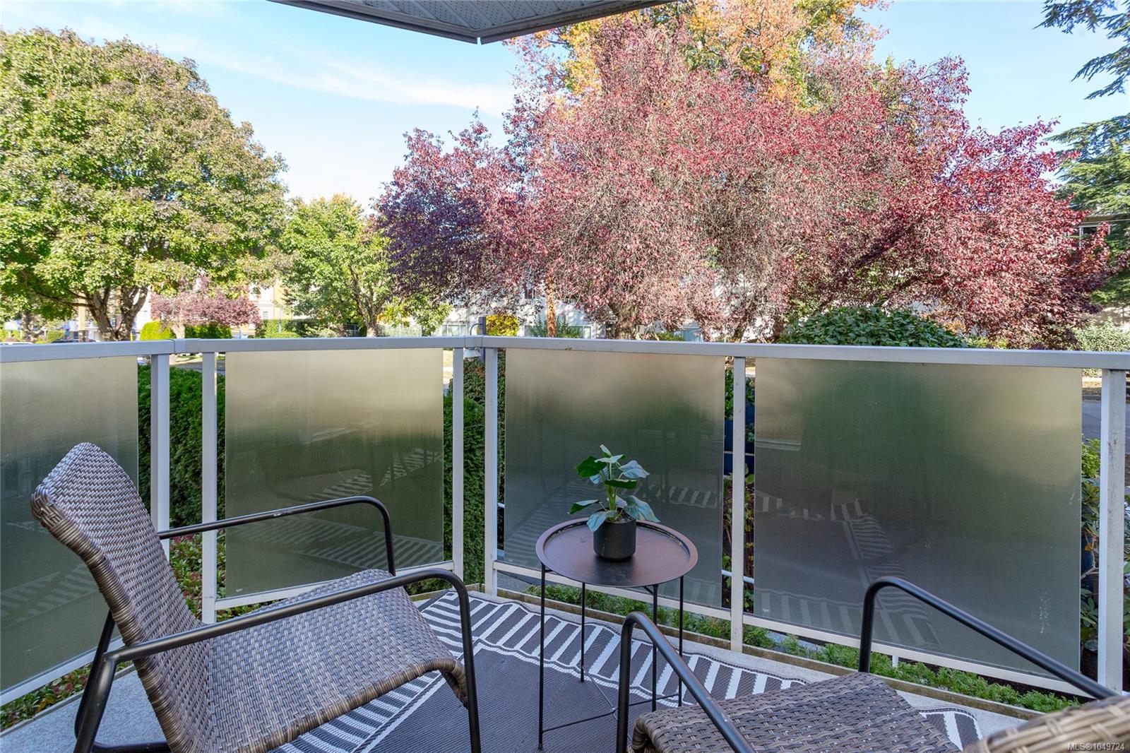 Condo balcony with woven chairs and a small table overlooking colorful autumn trees.