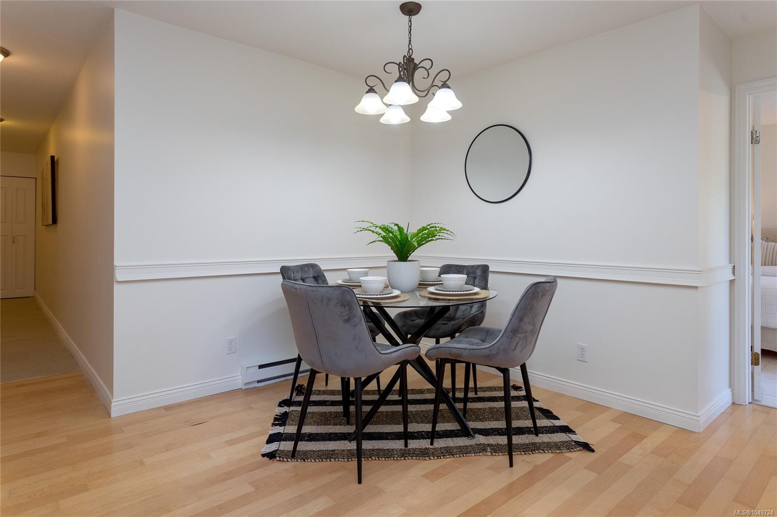 Dining area with a glass table, gray chairs, fern centerpiece, and chandelier.