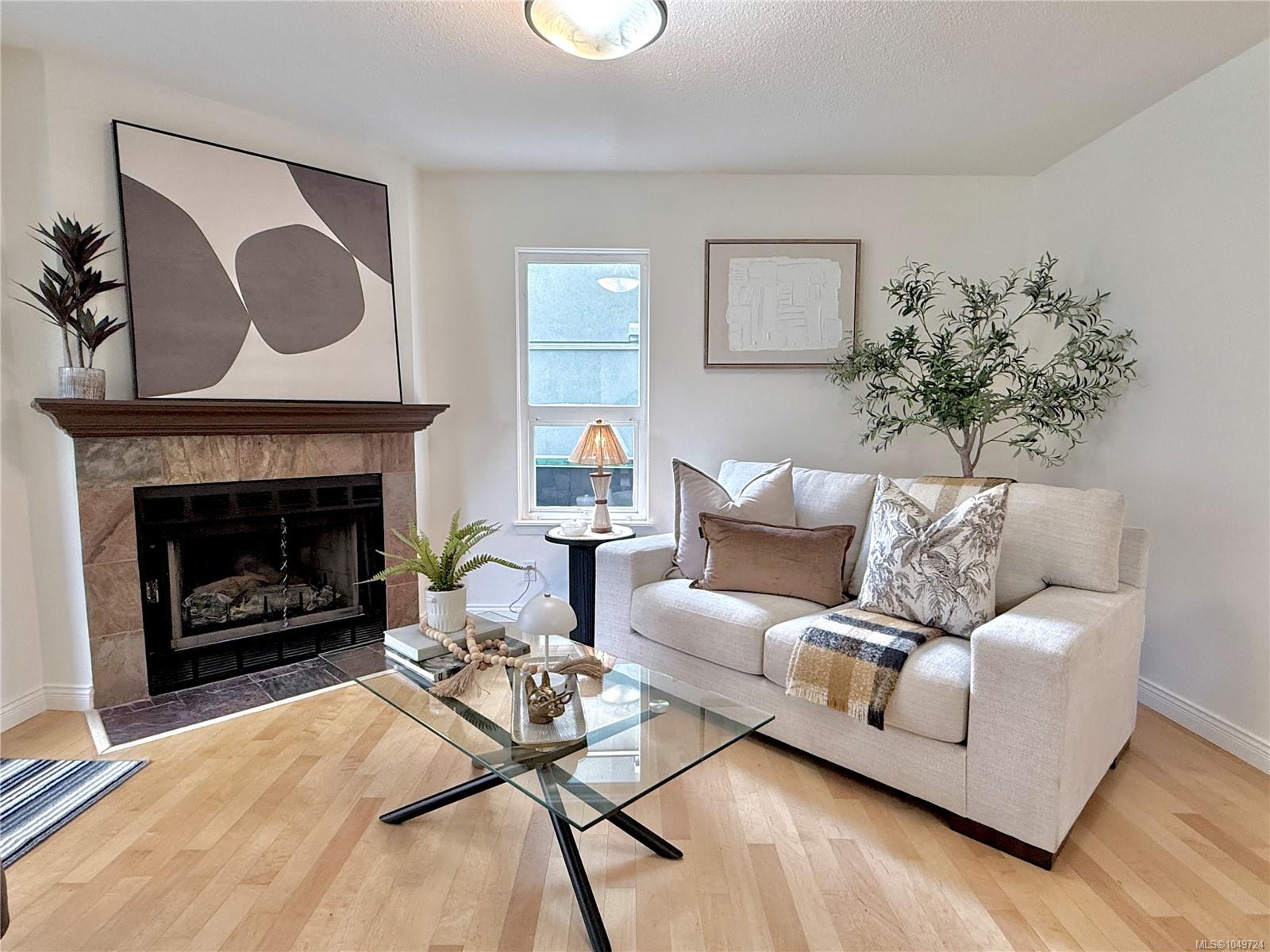 Staged living room with a cream sofa and glass coffee table beside a tiled fireplace.