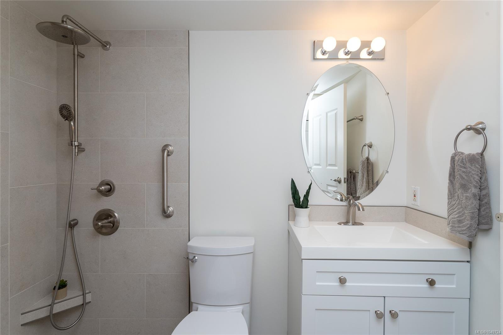 Updated bathroom with a gray-tiled walk-in shower, grab bars, and white vanity.