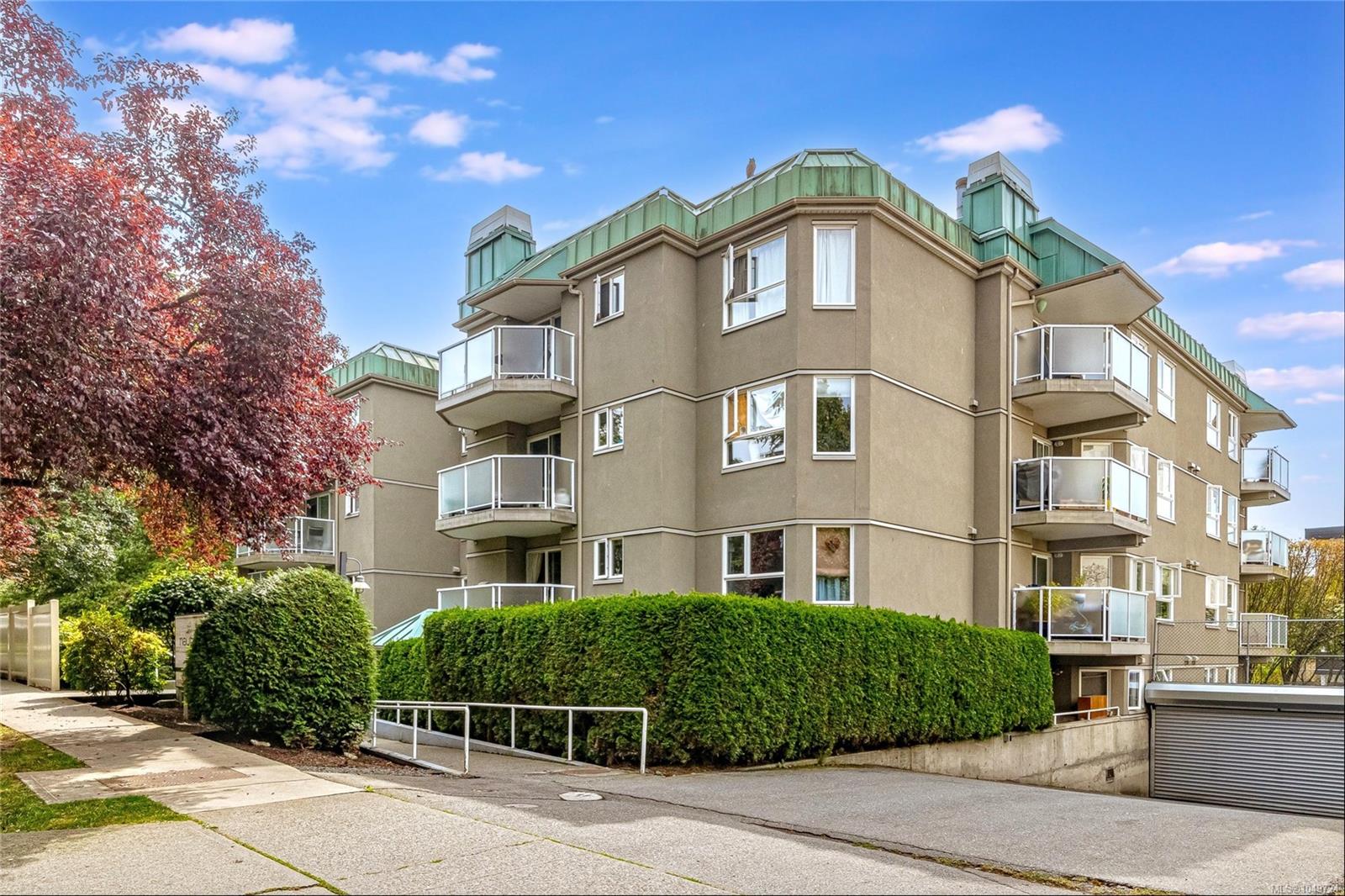 Condominium exterior with glass-railed balconies, green roof details, and autumn trees.