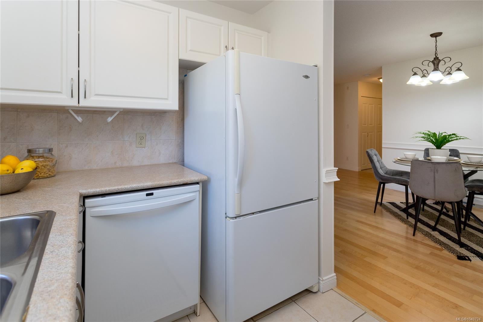 Kitchen with white cabinetry and refrigerator opening onto a dining area with a set table and gray chairs.