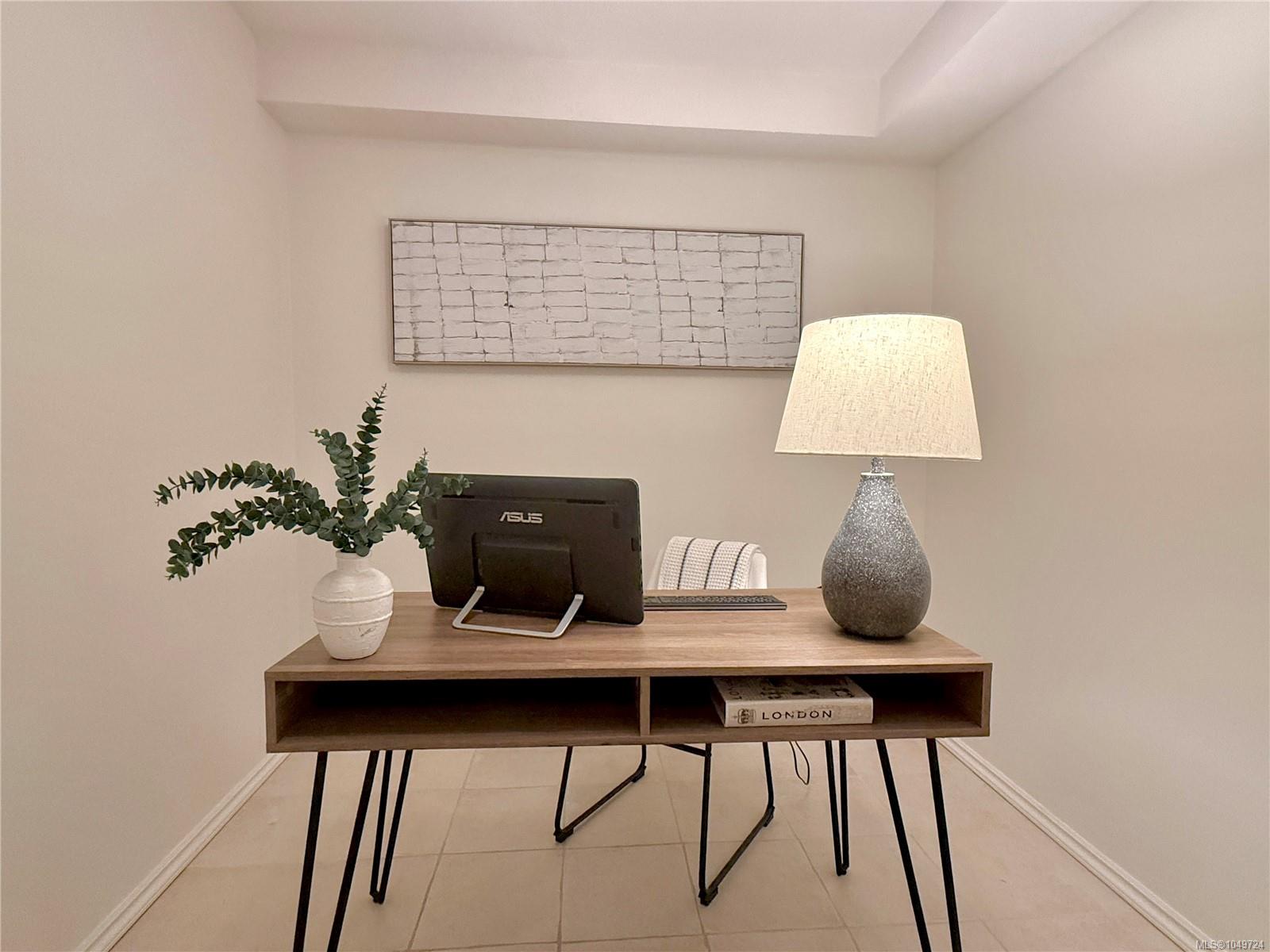 Staged home office nook with a wood desk, computer monitor, lamp, and potted plant.