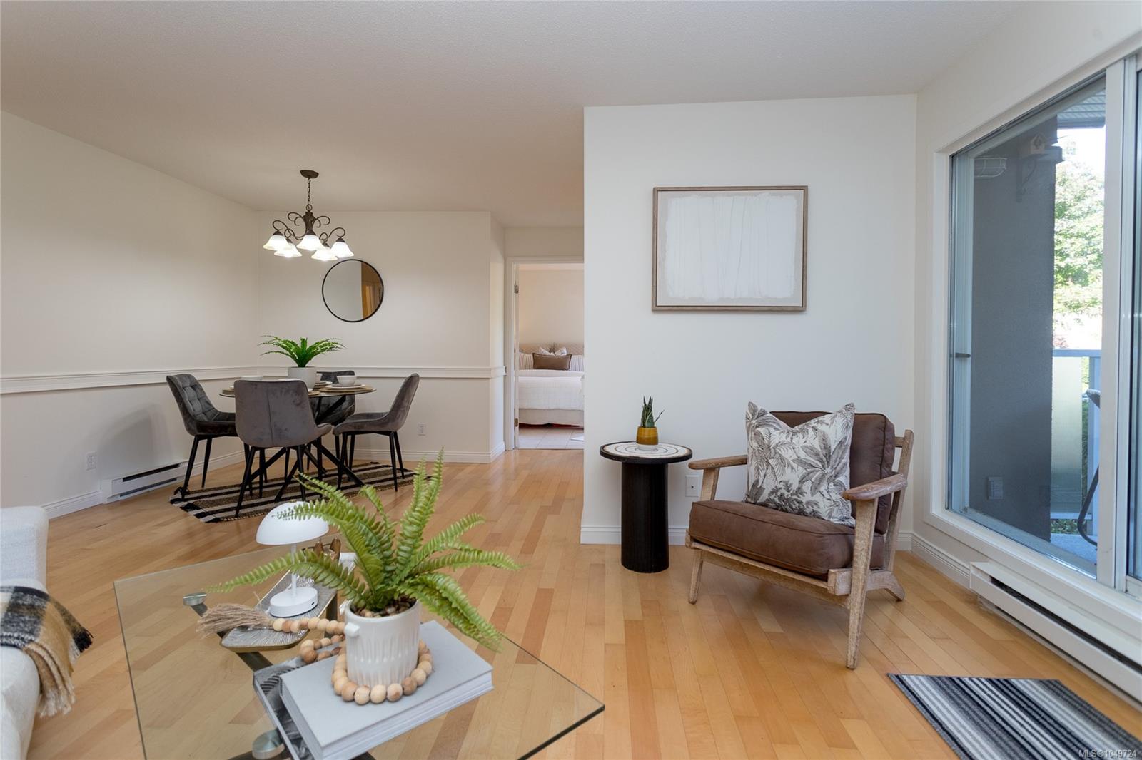 Condo living and dining area with hardwood floors, staged furniture, and sliding glass doors to a balcony.