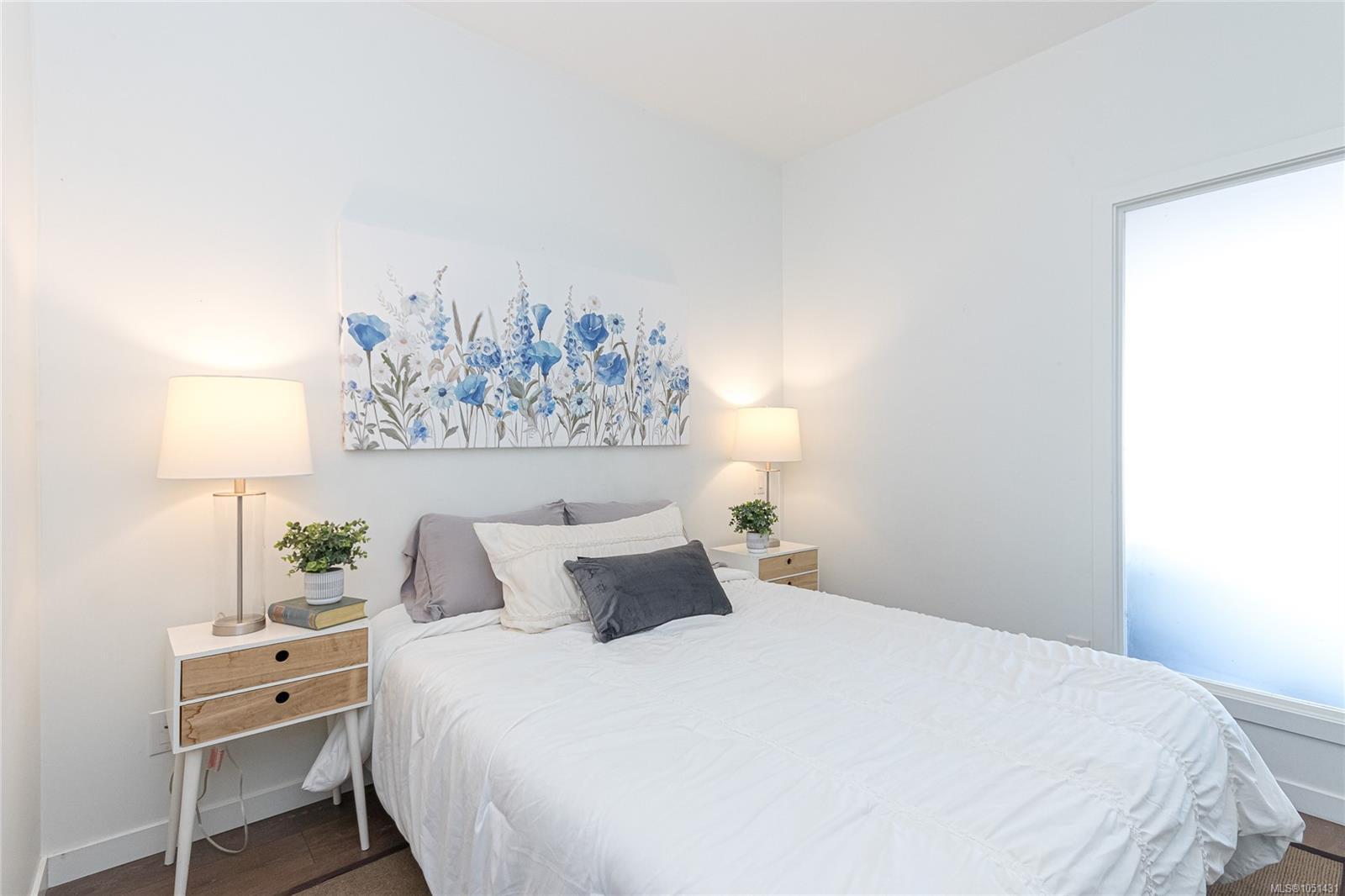 Staged bedroom with a white bed, blue floral wall art, and matching bedside tables and lamps.