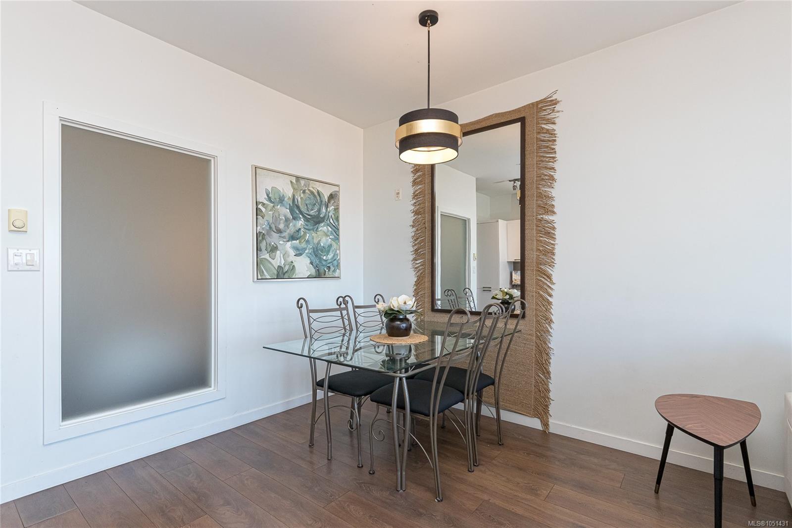 Staged condo dining area with a glass table, metal chairs, and a tall fringed mirror.