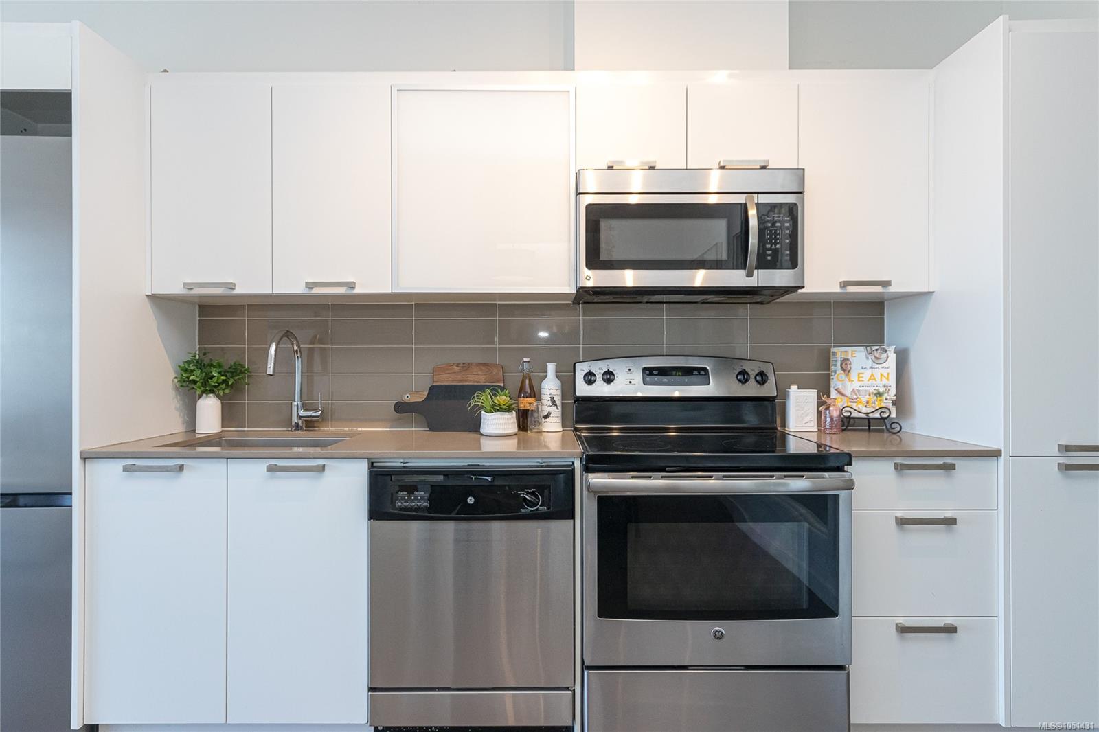 Modern white kitchen with stainless steel appliances, gray tile backsplash, and a countertop sink.