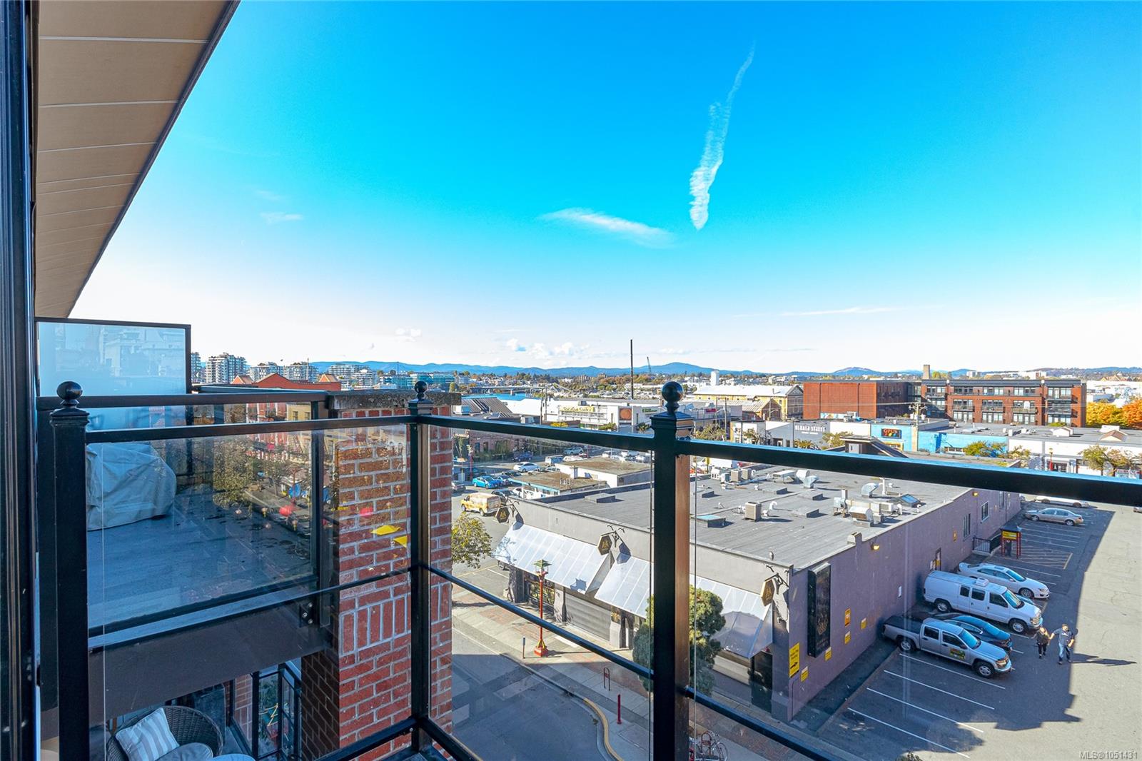 Condo balcony overlooking downtown rooftops and distant hills on a sunny day.