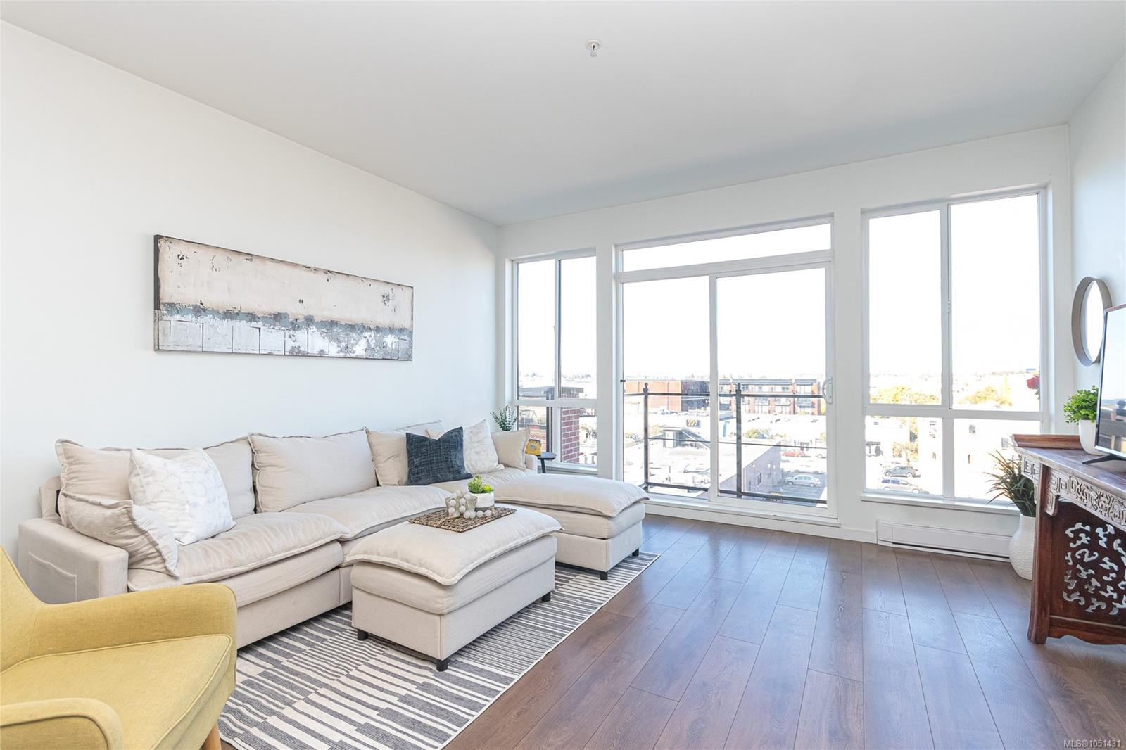 Bright living room with a cream sectional and large windows overlooking nearby buildings.