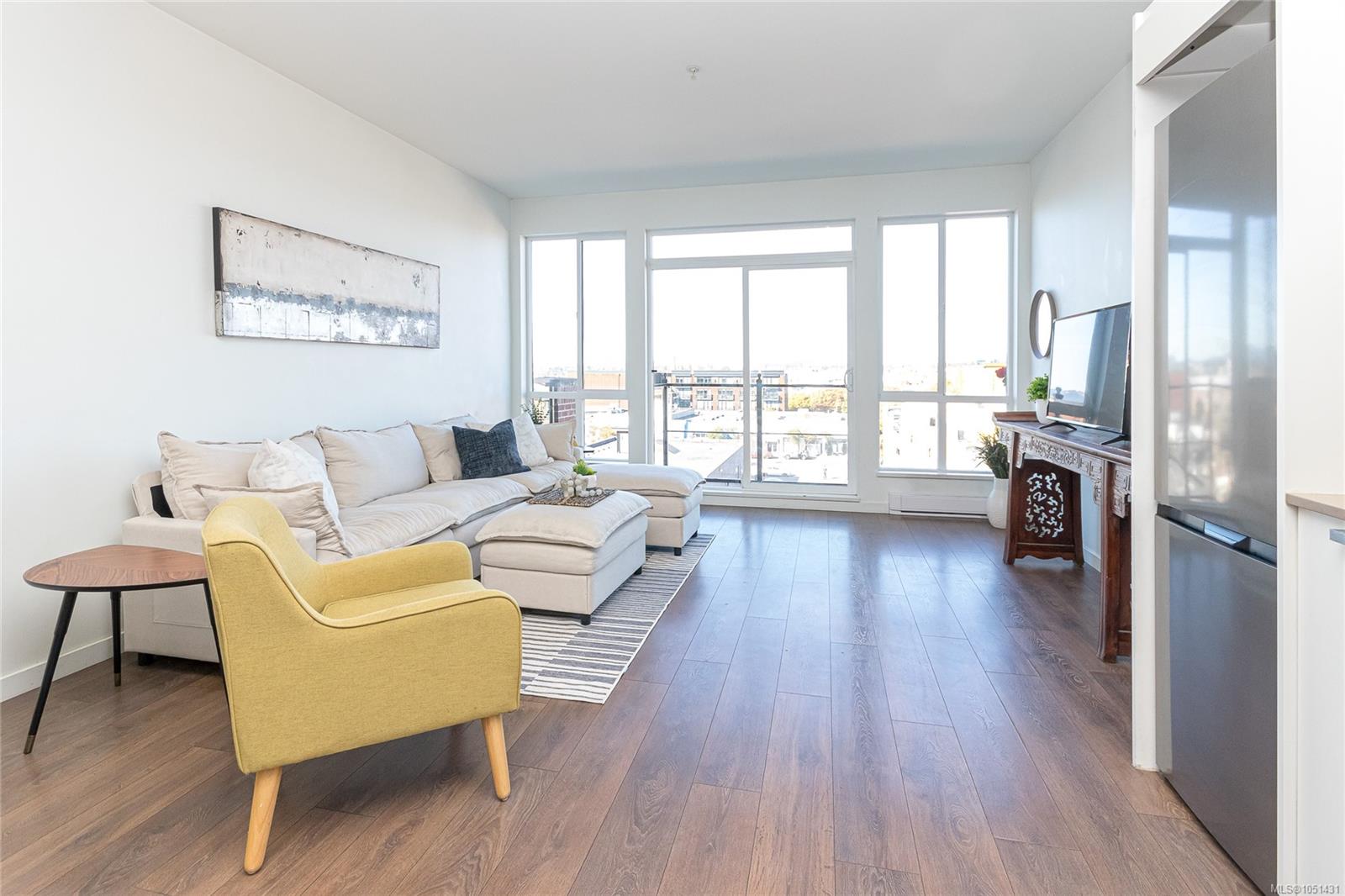 Furnished living room with a cream sectional, yellow accent chair, and large windows overlooking nearby buildings.
