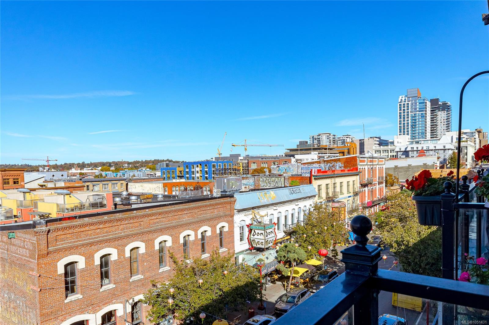 Downtown Victoria view from a balcony, overlooking brick storefronts and high-rises beneath a clear blue sky.