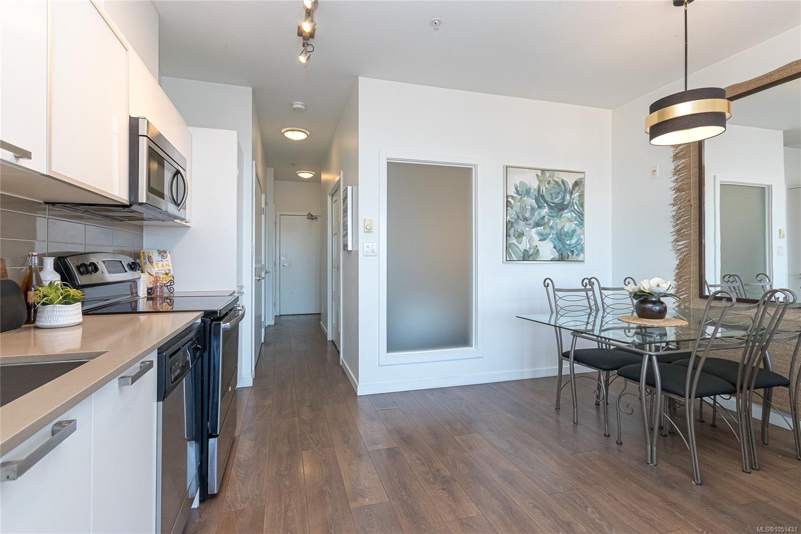 Furnished condo kitchen and dining area with stainless-steel appliances, glass table, and wood-look flooring.