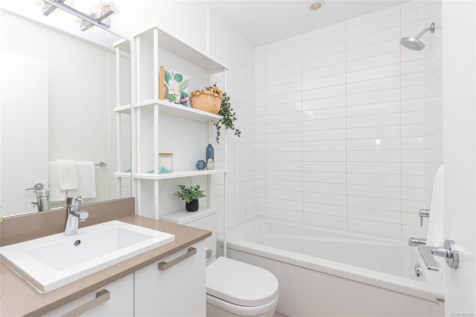 Bathroom with a tiled tub, white vanity, tan countertop, and open decorative shelving.