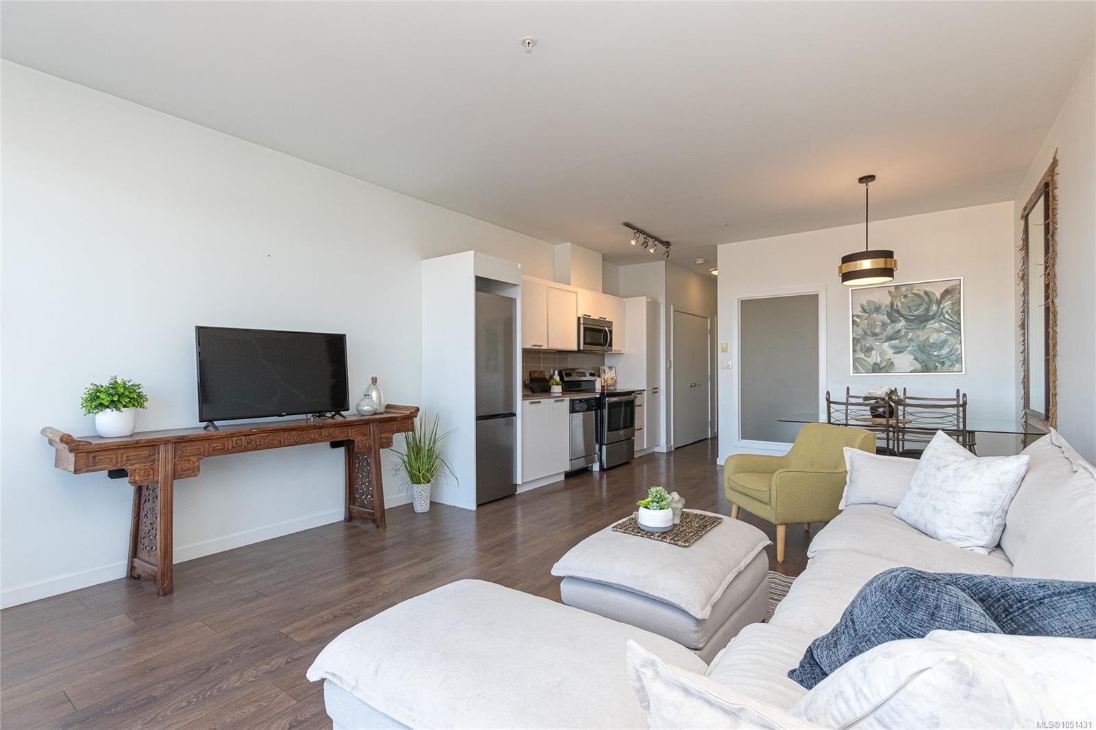 Open-plan condo living room with a white sectional, carved wood console, and stainless steel kitchen.