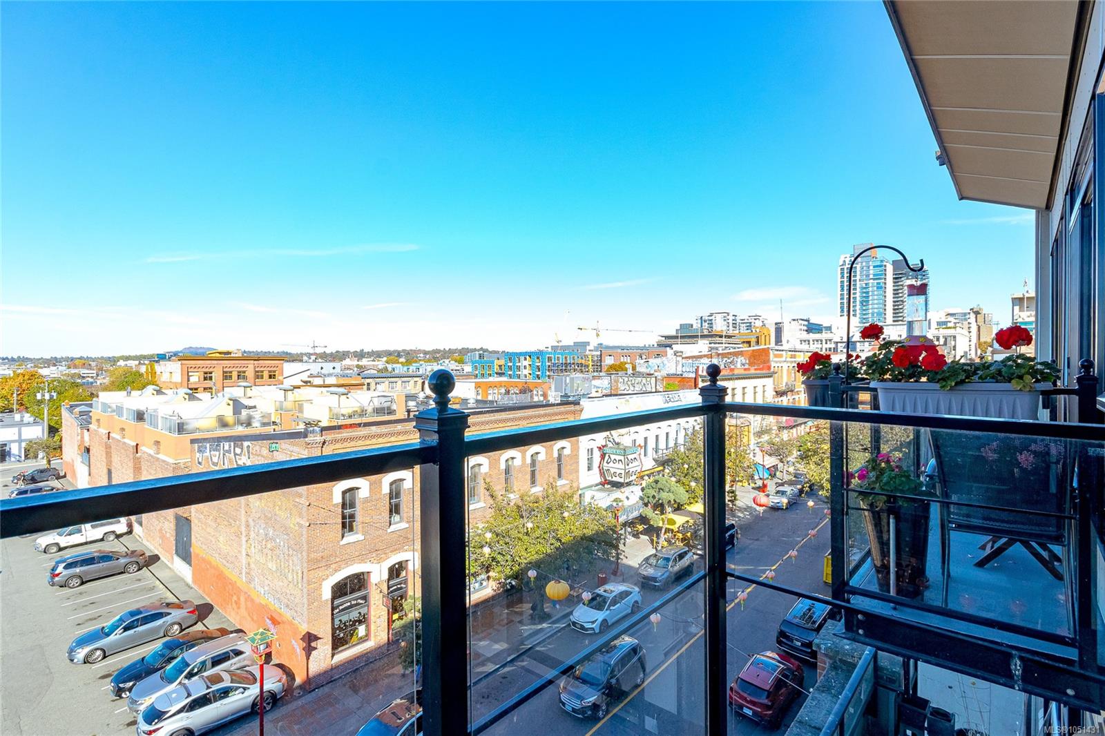 Condo balcony overlooking downtown Victoria, with glass railings and red flowers in planters.