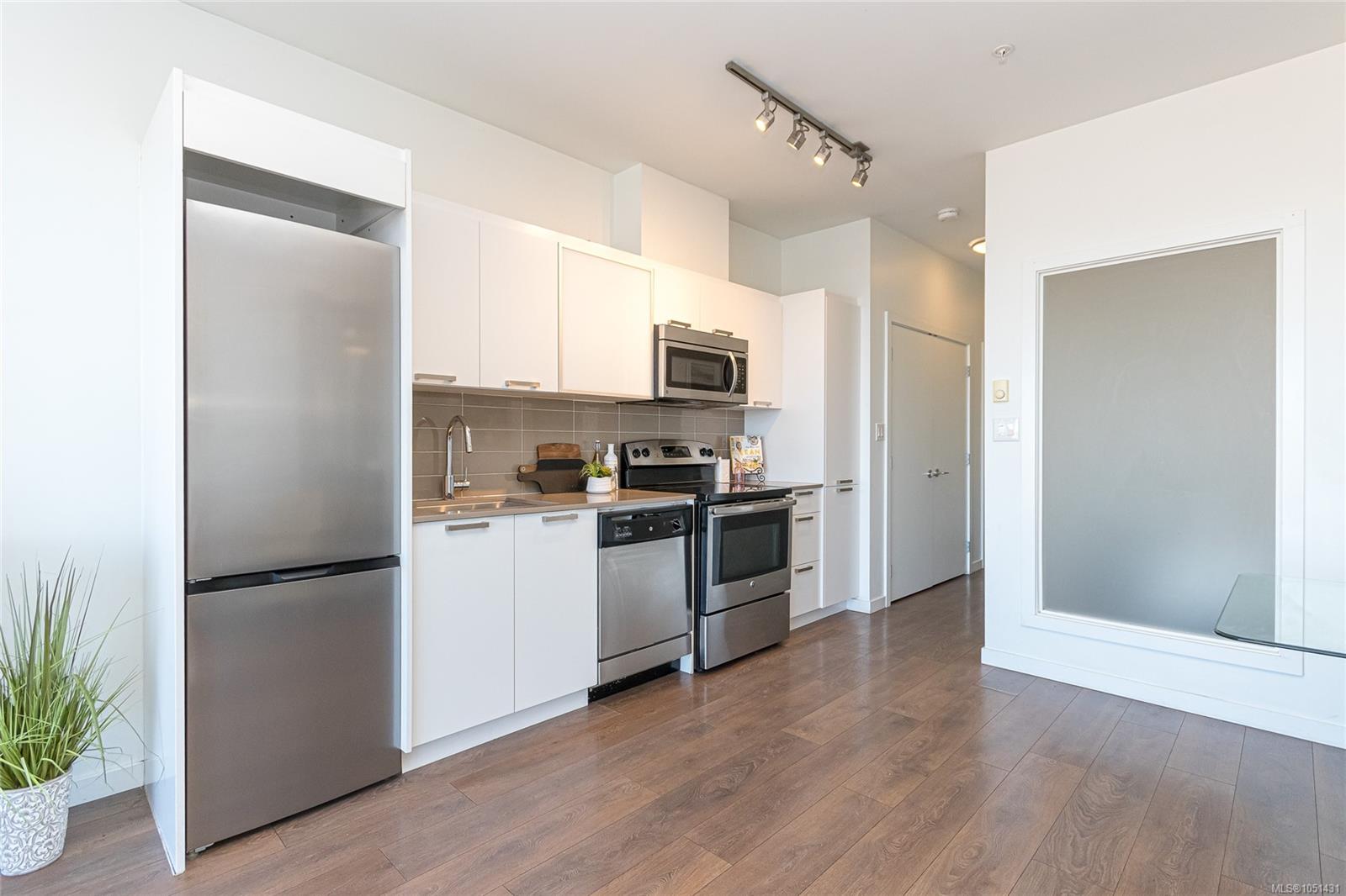 Condo kitchen with white cabinetry, stainless steel appliances, and warm wood flooring.