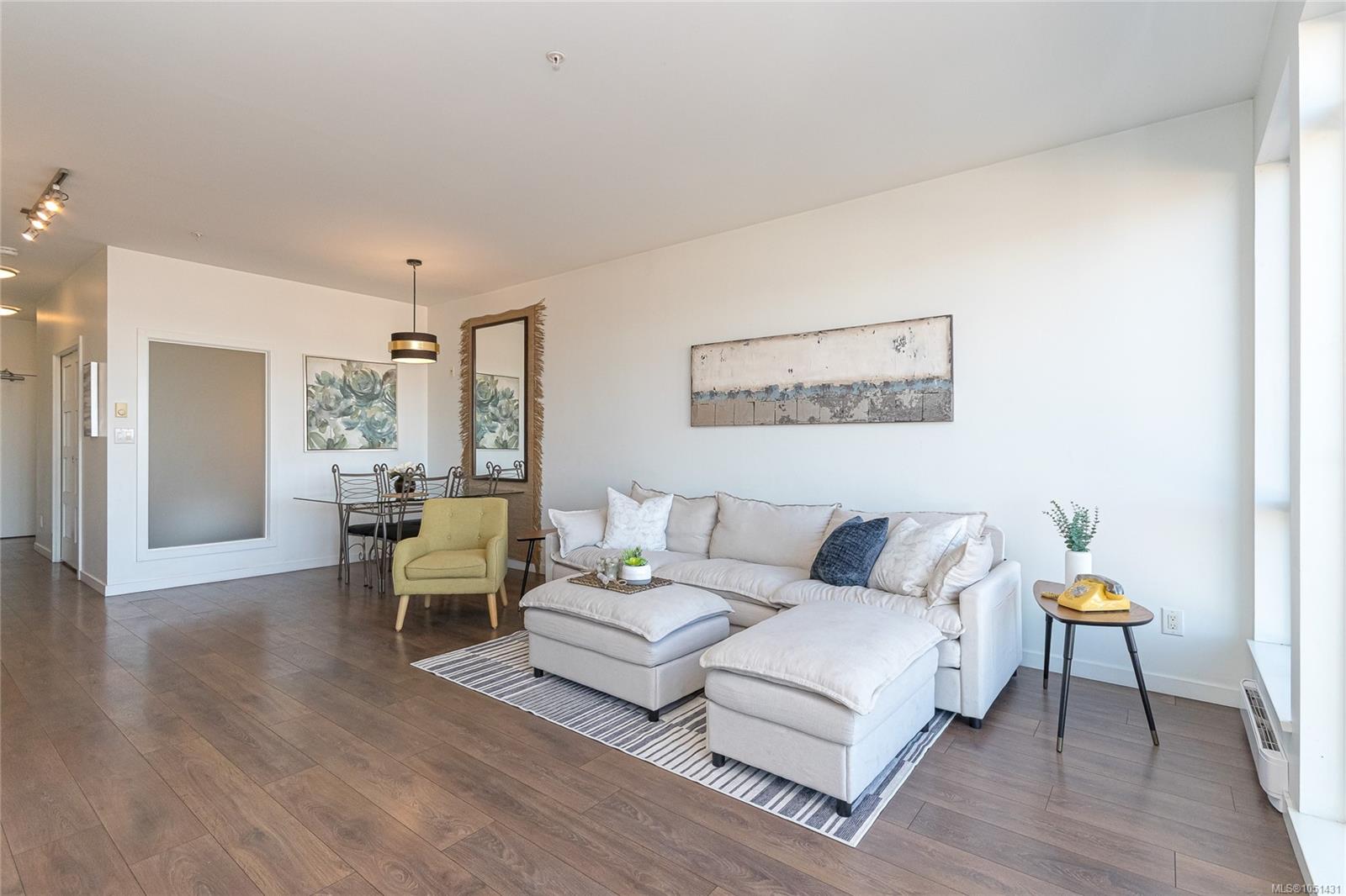 Bright condo living room with a white sectional, green chair, dining area, and wood-look floors.
