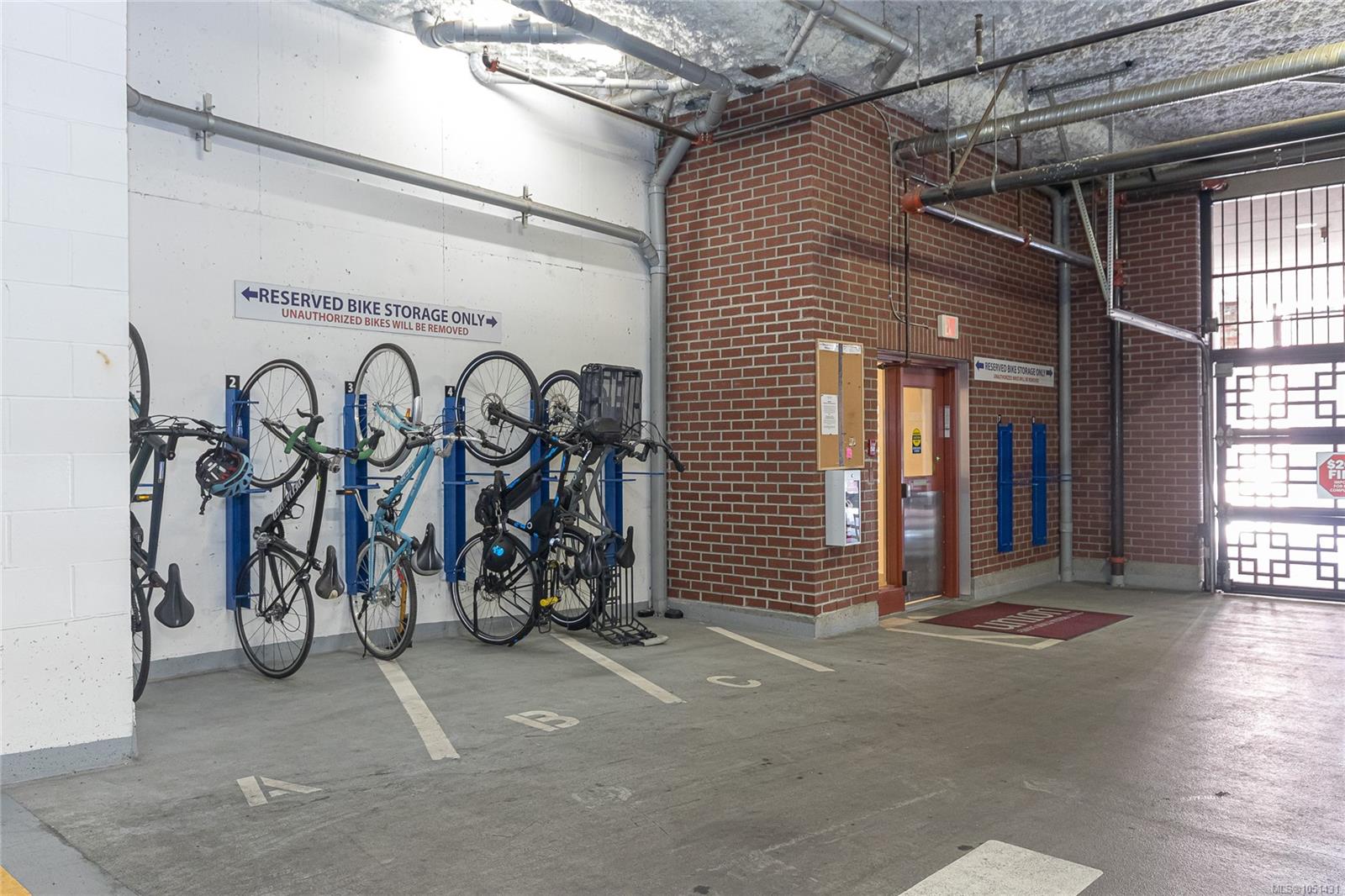 Indoor bicycle storage area with wall-mounted racks beside a brick elevator enclosure.