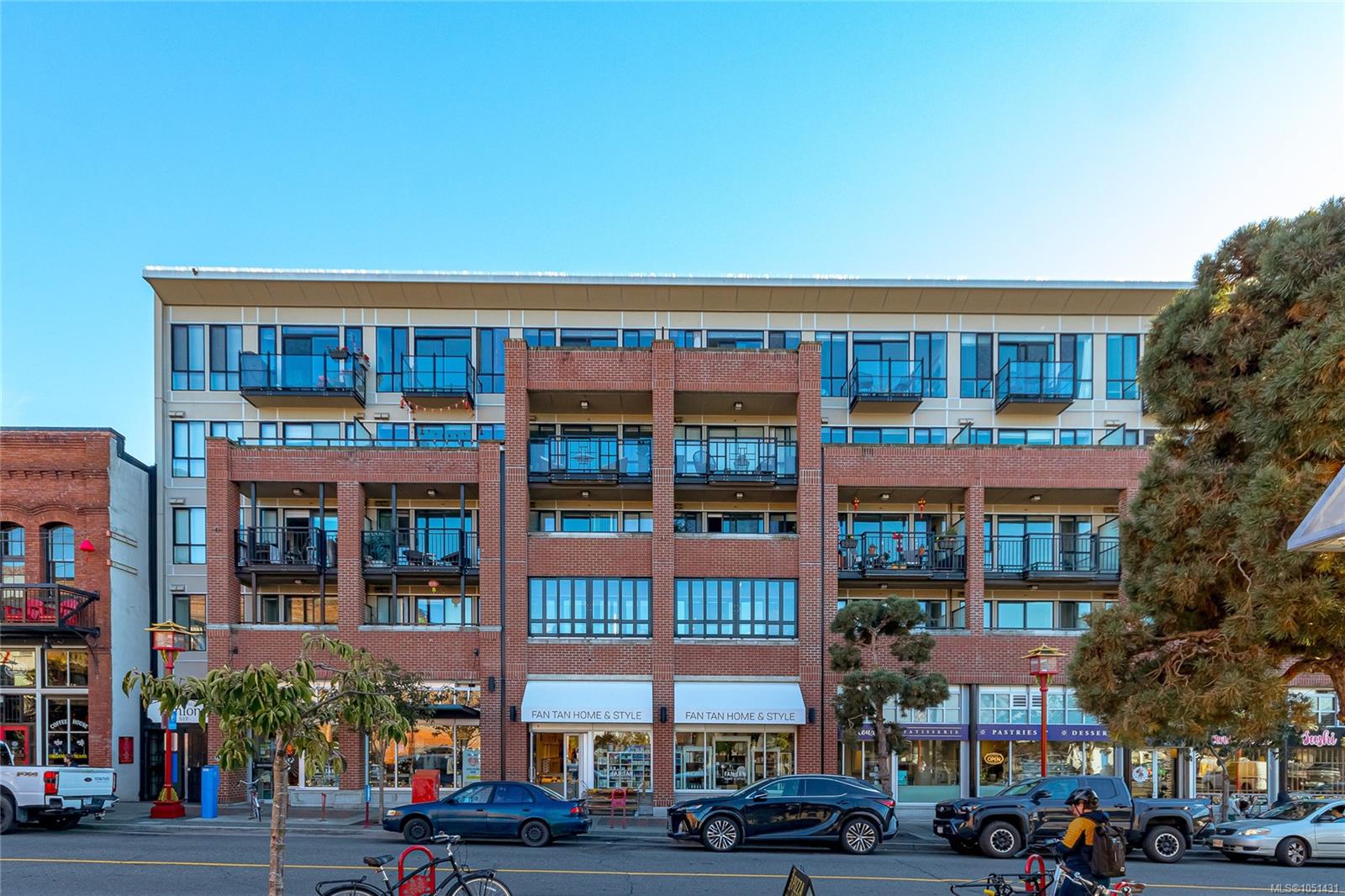 Mixed-use building with a red-brick facade, glass balconies, and street-level shops.