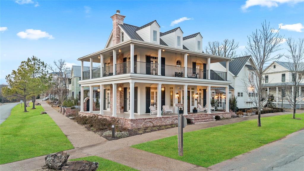 White two-story house with a wraparound porch, upper balcony, and brick accents.