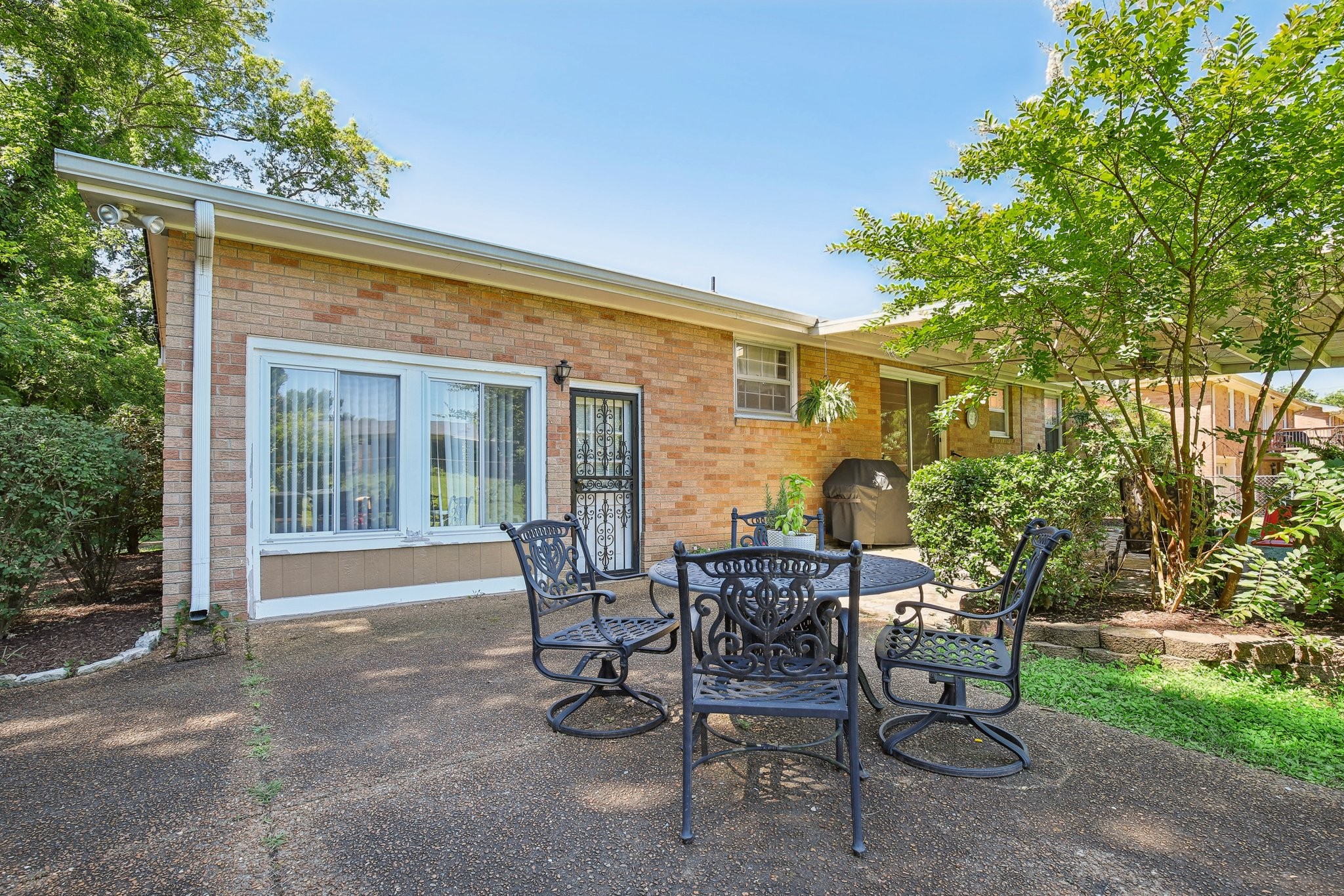 Brick home patio with black metal dining furniture beneath mature trees.