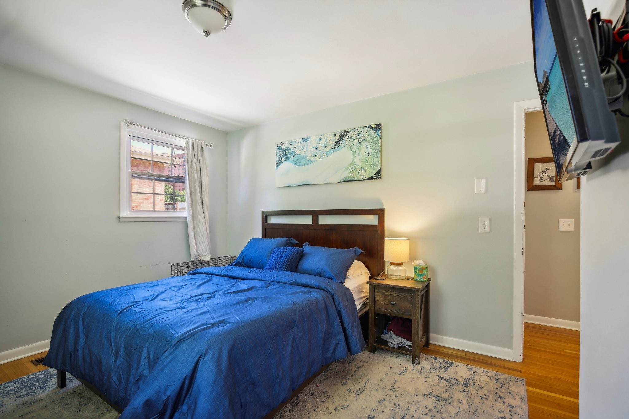 Bedroom with bright blue bedding, dark wood headboard, and a curtained window.