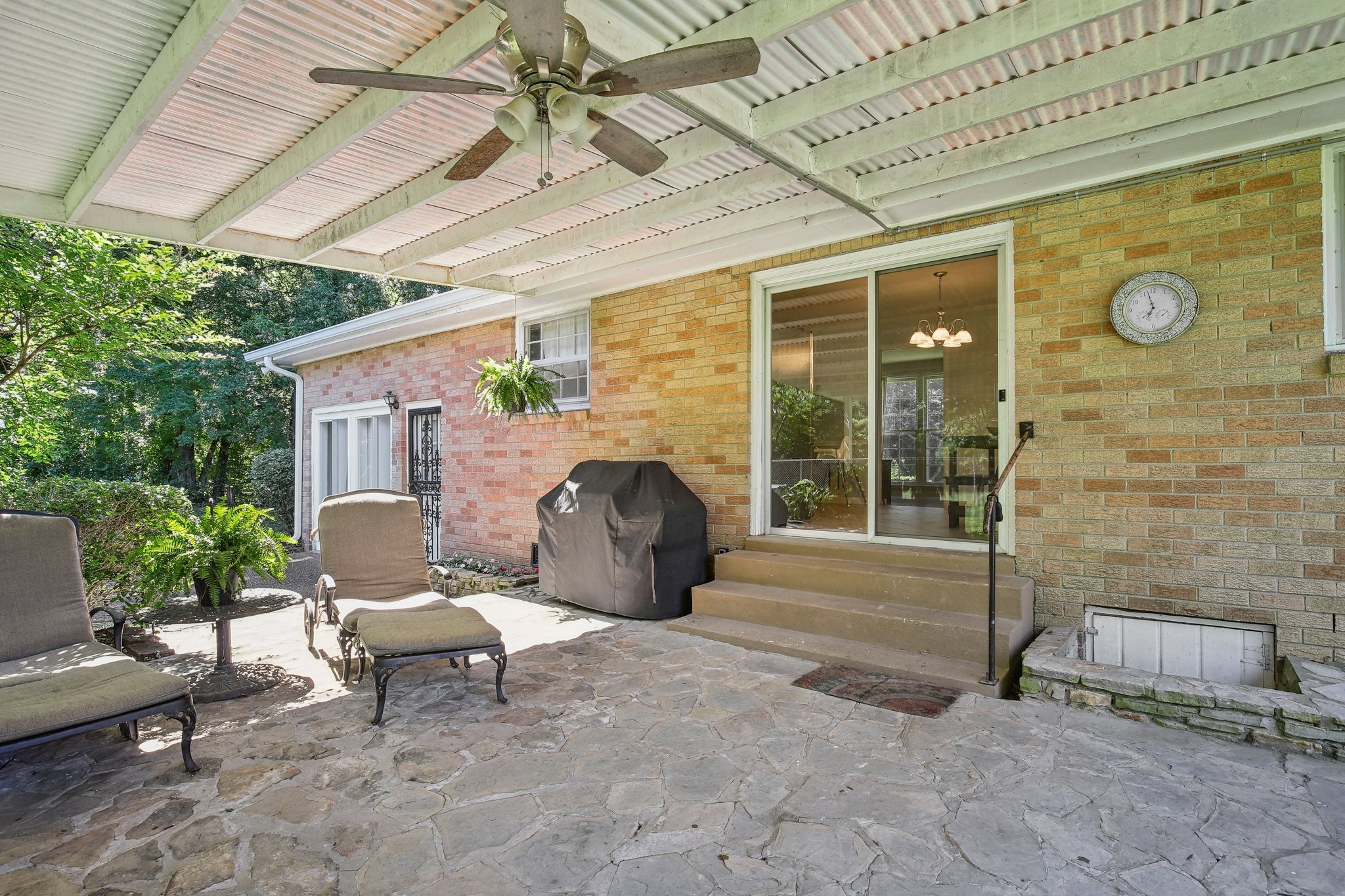 Covered stone patio with lounge chairs, a ceiling fan, and sliding glass doors.