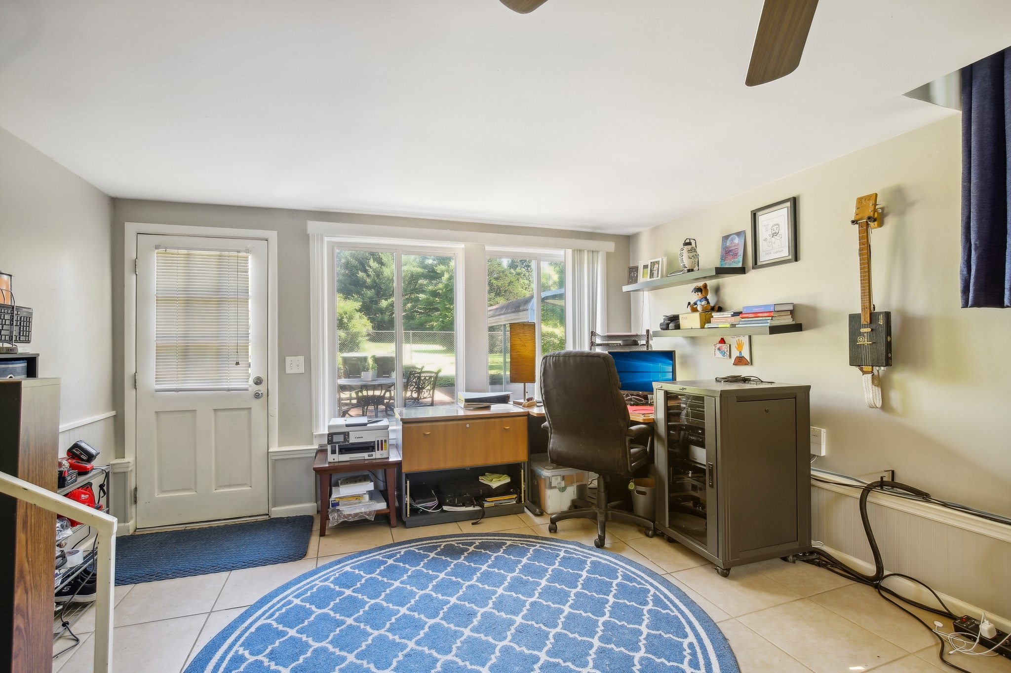 Home office with a desk and computer beside large windows and a sliding glass door.