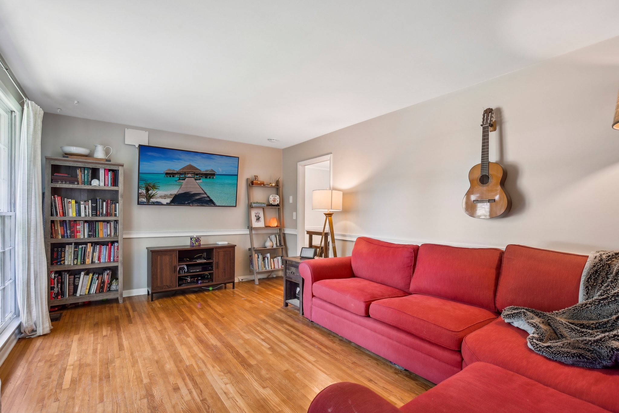 Living room with a red sectional sofa, hardwood floors, bookshelves, and a guitar on the wall.