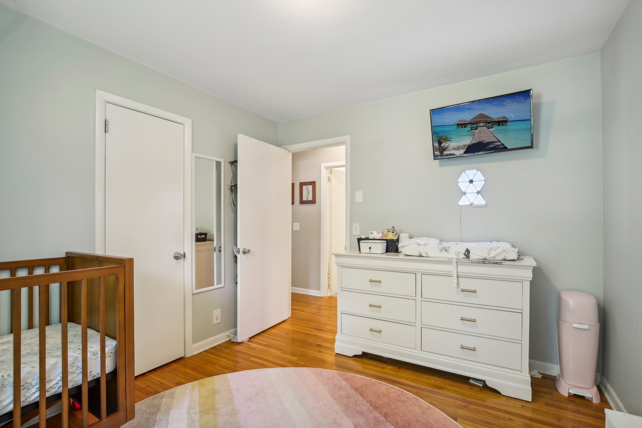 Nursery with a wooden crib, white dresser and changing pad, and a pastel round rug.