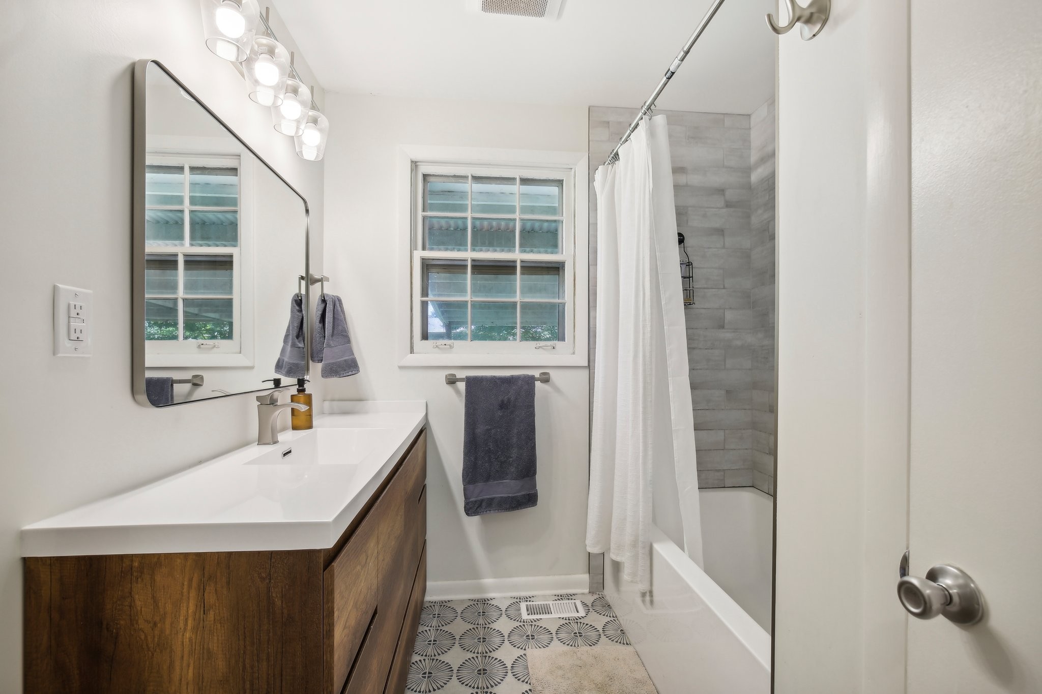 Bathroom with a wood vanity, patterned tile floor, and gray-tiled tub-shower.