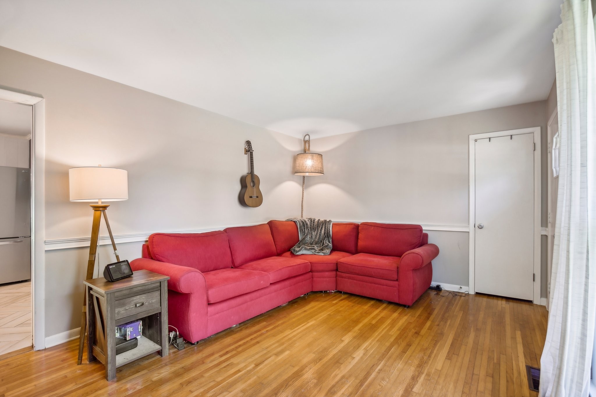 Living room with a red sectional sofa, hardwood floors, and a guitar on the wall.