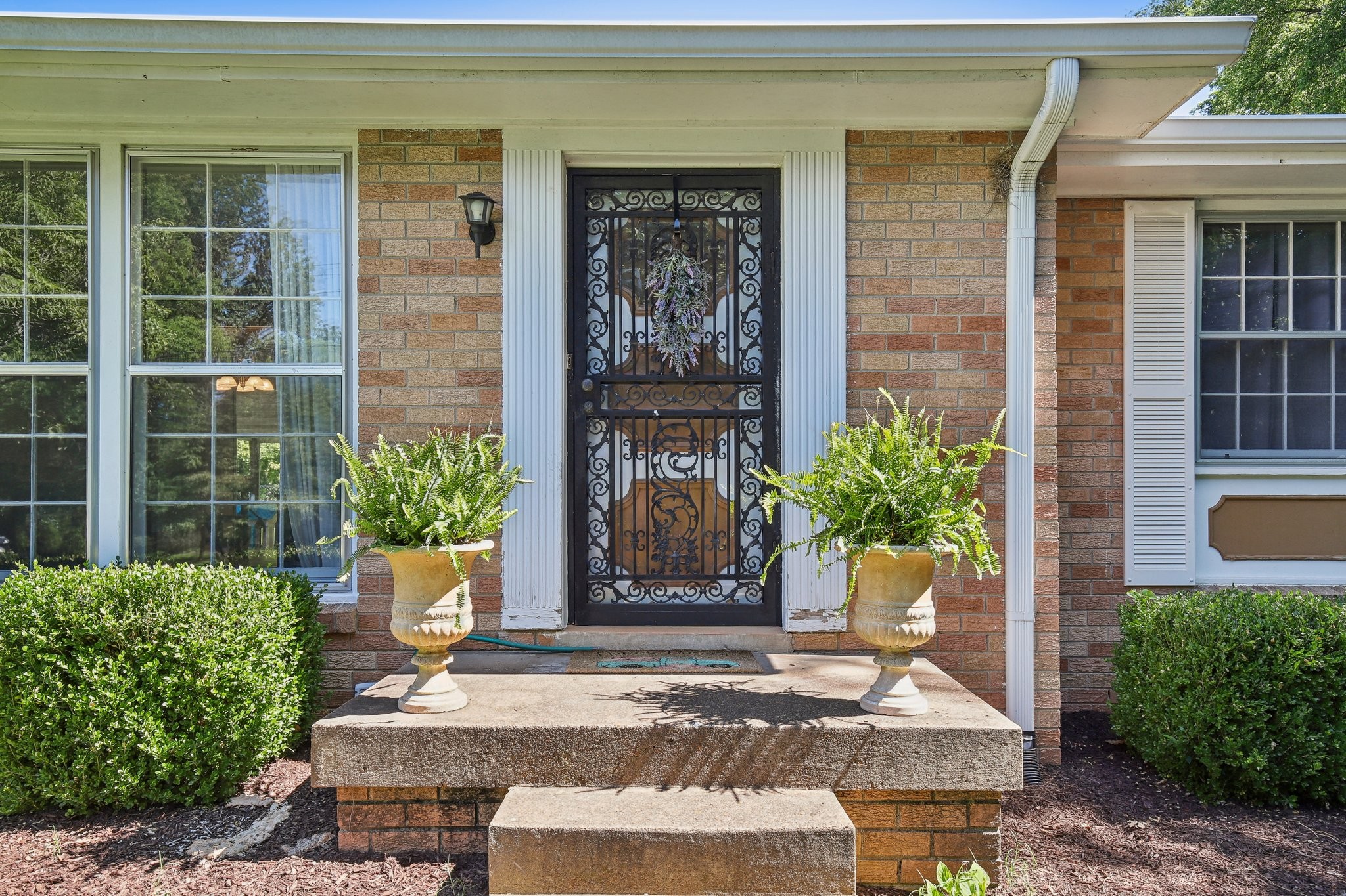 Brick home entrance with ornate black security door and matching fern planters beside the steps.