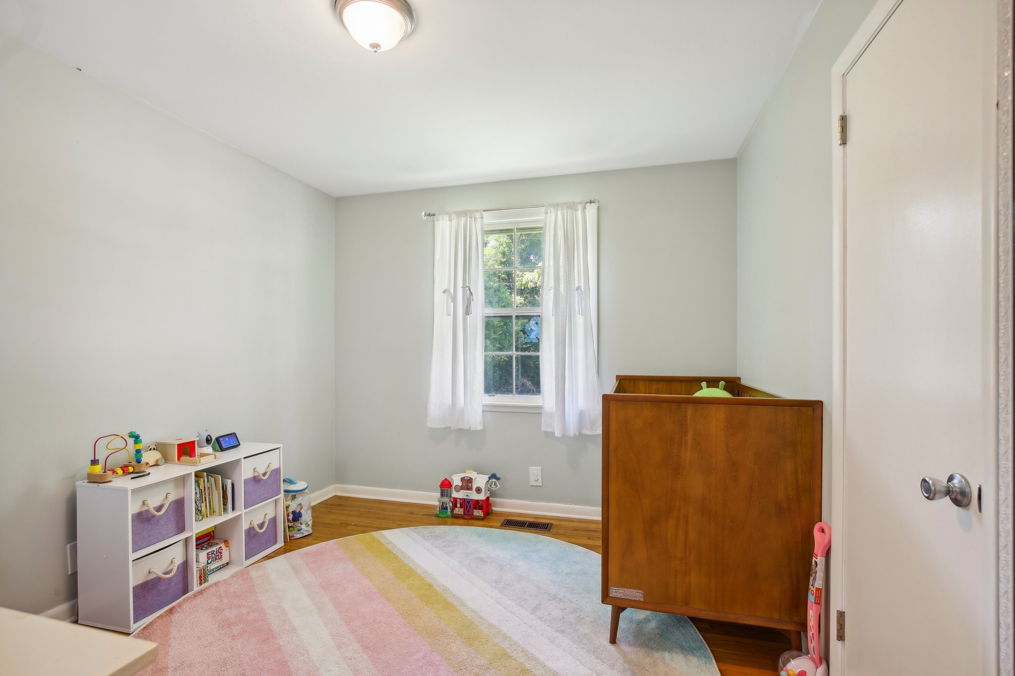 Nursery with a wooden crib, toy shelves, and a pastel striped rug.