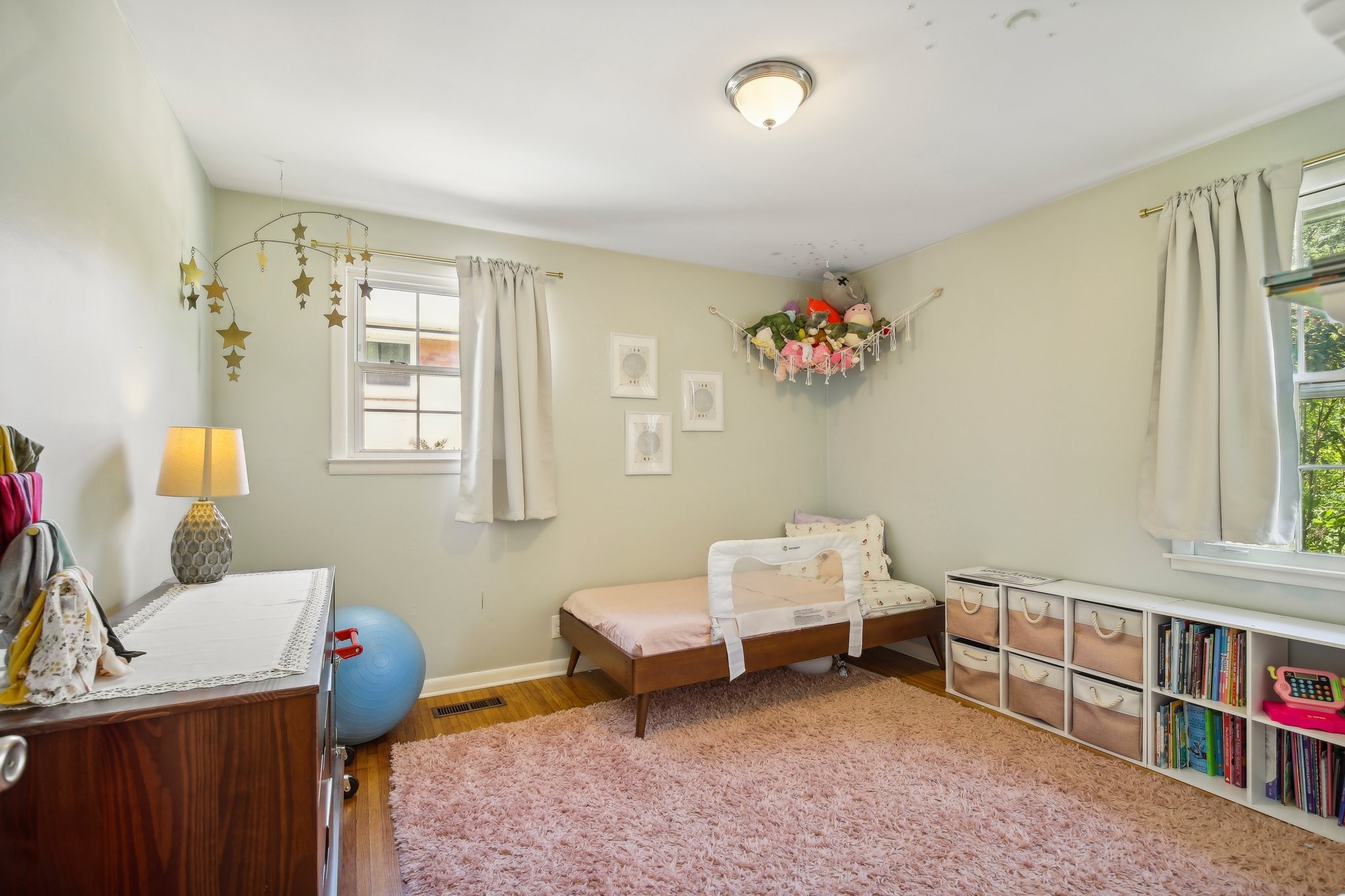 Nursery with a toddler bed, plush toys in a wall hammock, and a large pink rug.