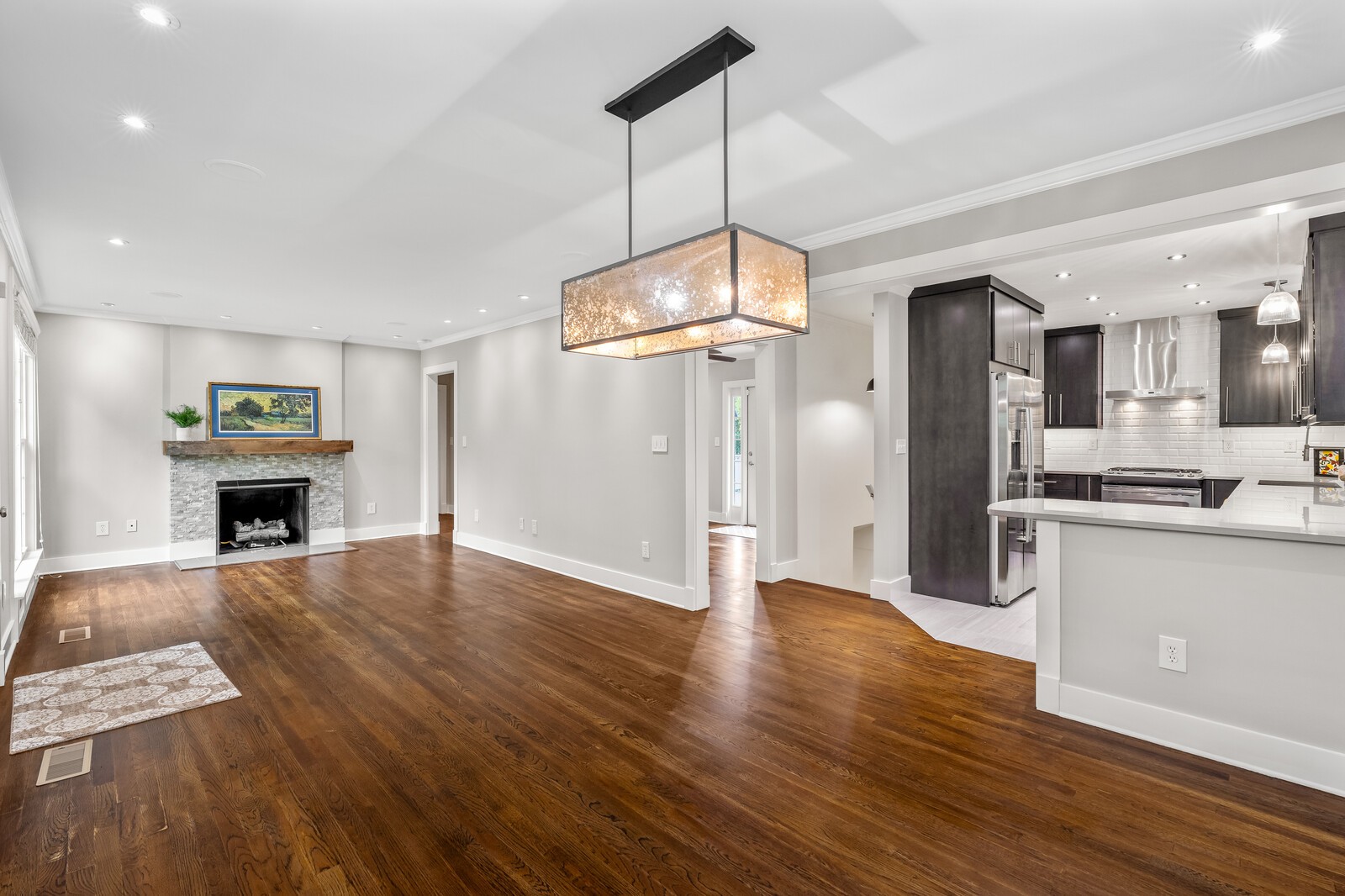 Open-plan living room and kitchen with hardwood floors, stone fireplace, and dark cabinetry.