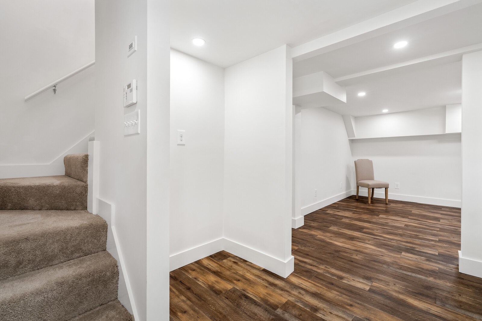 Finished room with dark wood floors, built-in shelving, a chair, and carpeted stairs.