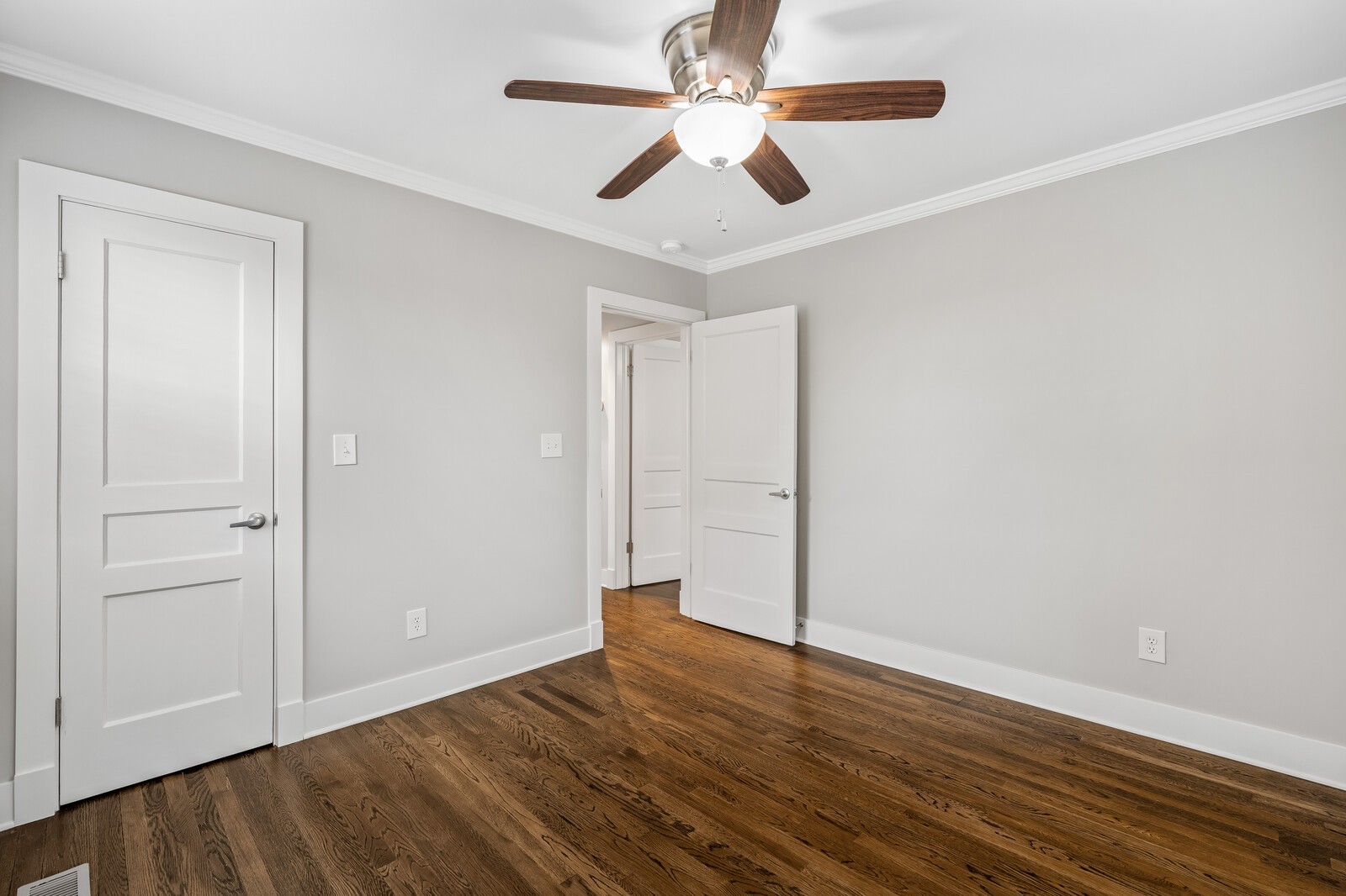 Empty room with dark hardwood floors, gray walls, and a wood-blade ceiling fan.