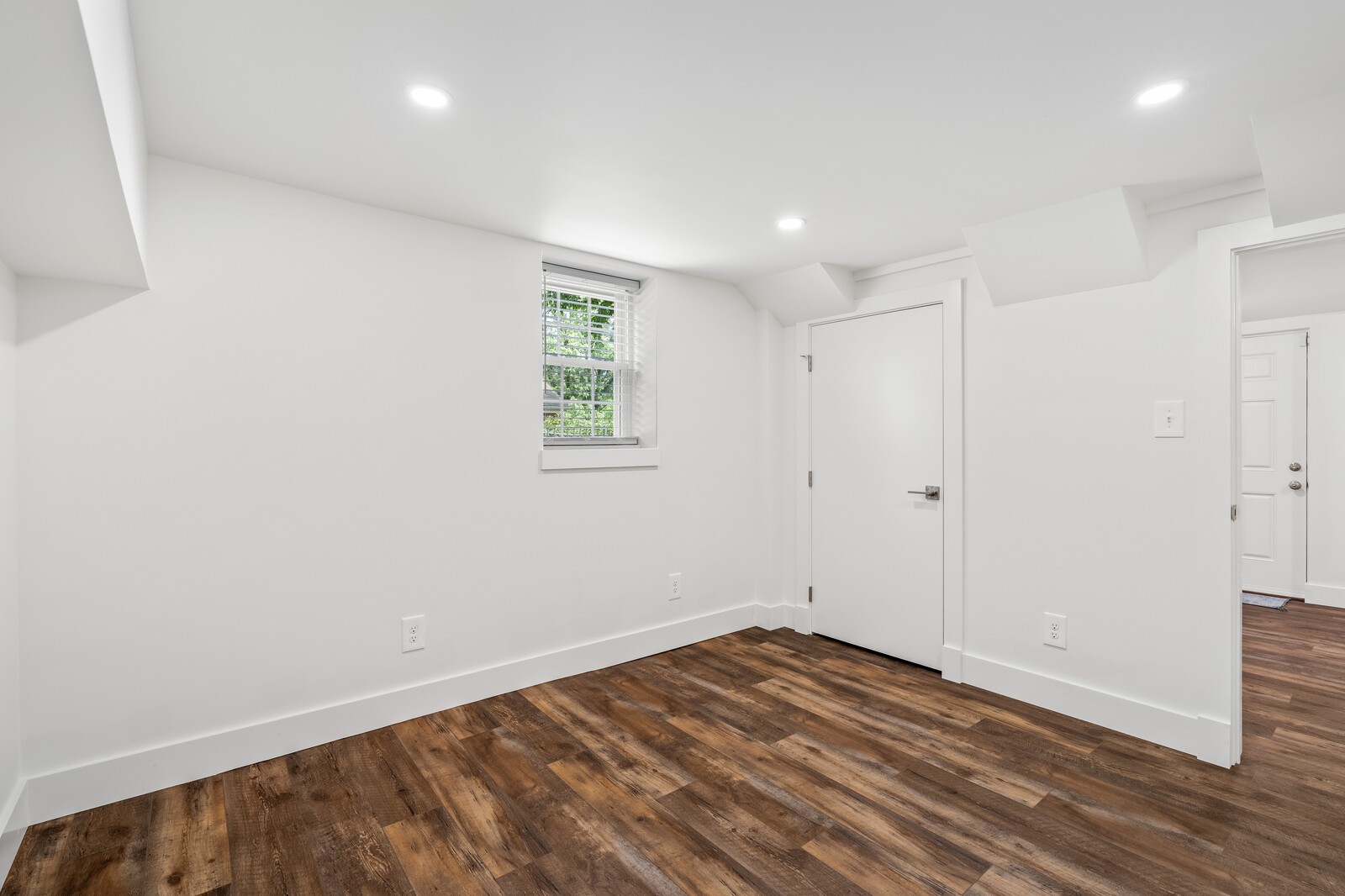 Empty room with dark wood-look flooring, a small window, and a low angled ceiling.