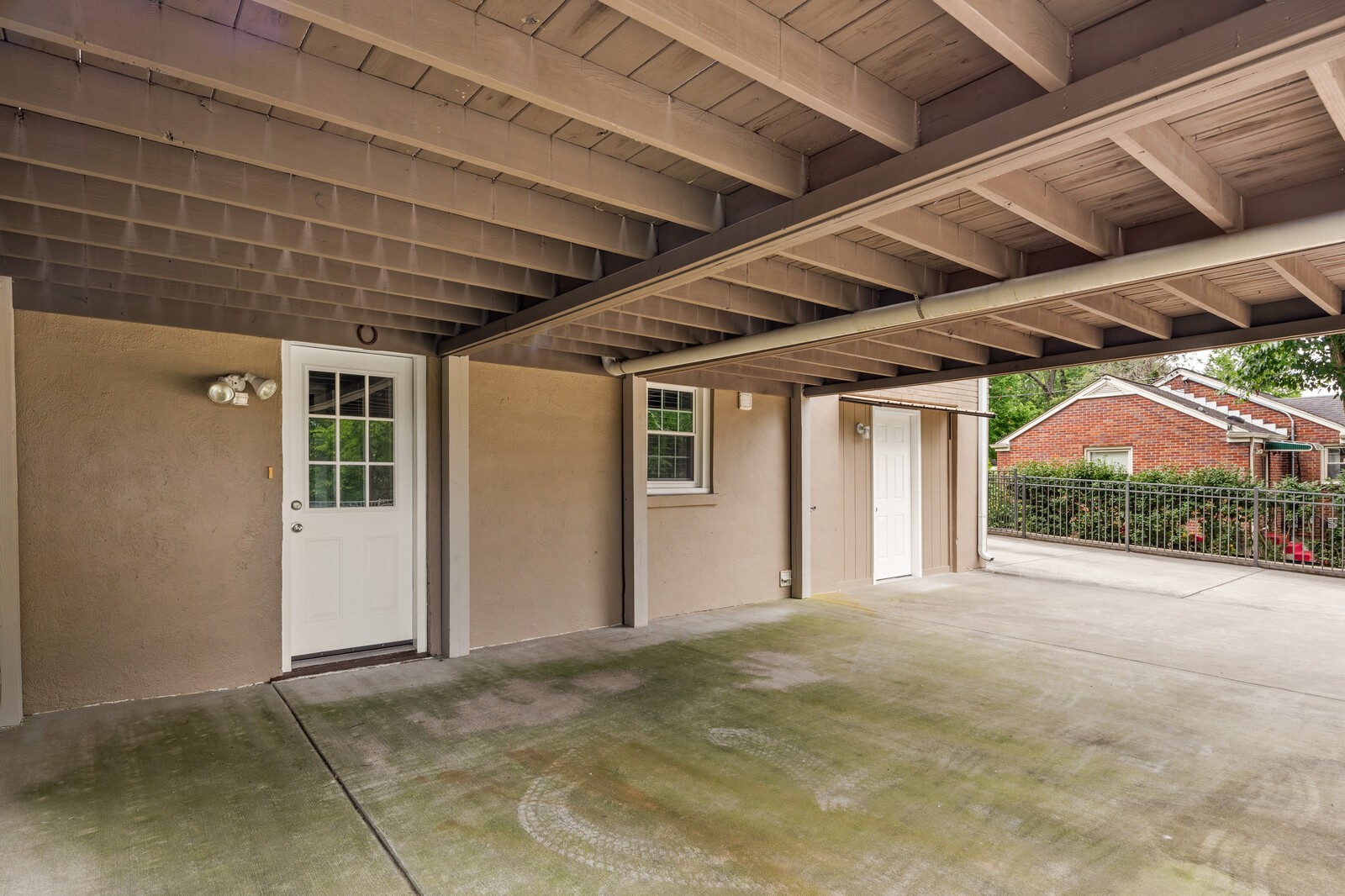 Covered concrete patio beneath a wood deck, with two white doors and a black metal railing.