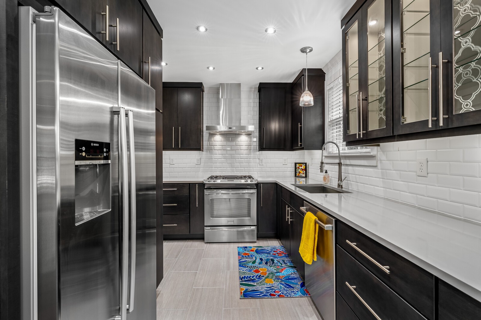 Kitchen with dark cabinets, white subway tile, stainless steel appliances, and a colorful runner rug.
