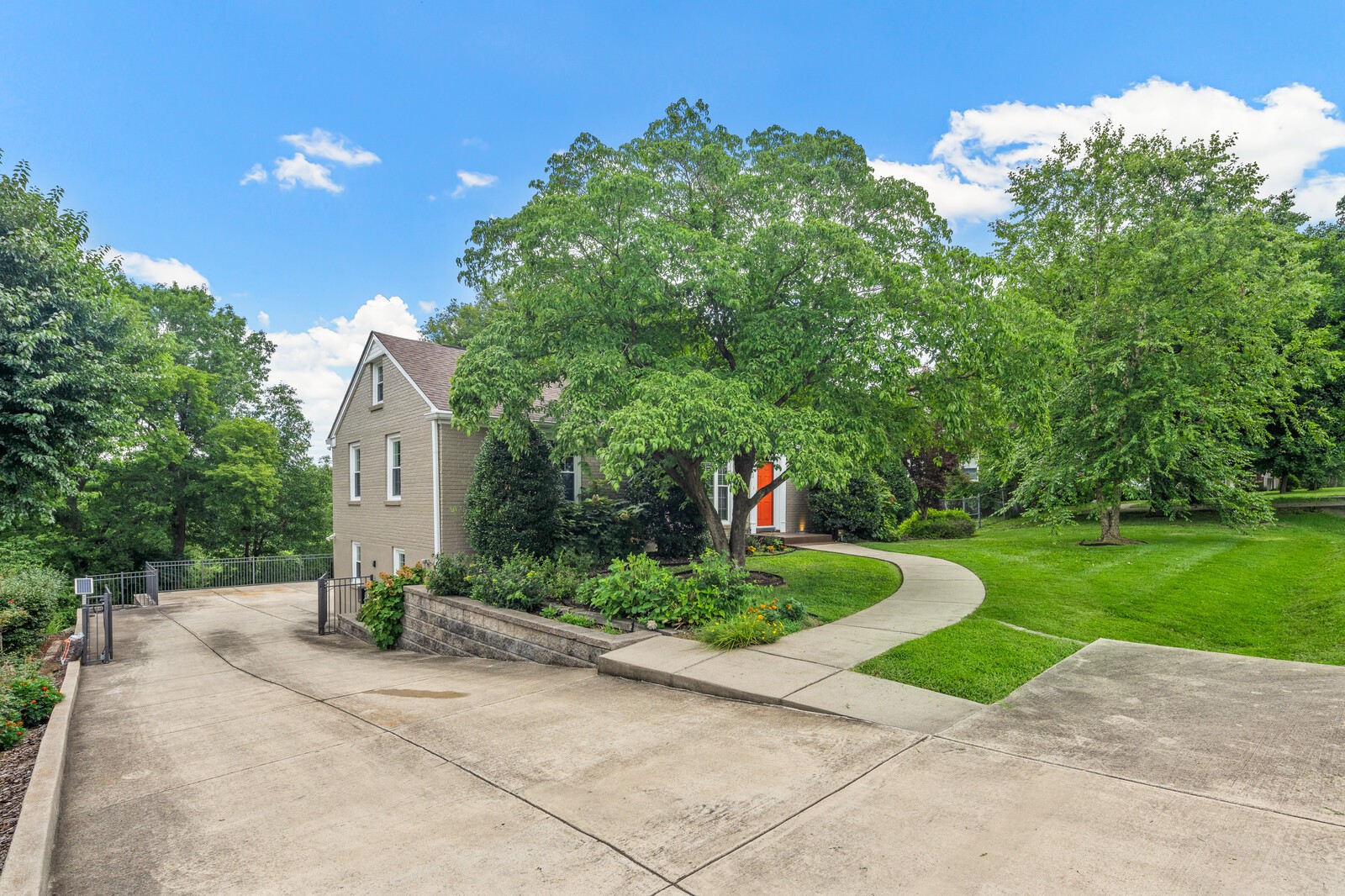 Two-story home with an orange front door, curved walkway, landscaped lawn, and wide concrete driveway.
