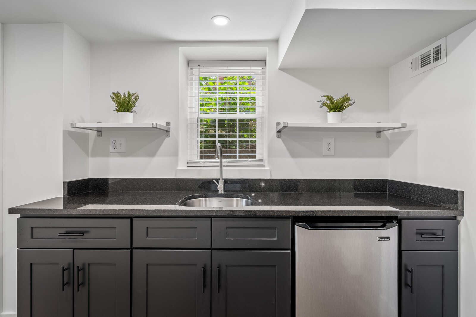Kitchen with dark cabinets, black stone countertops, and a sink beneath a window with white blinds
