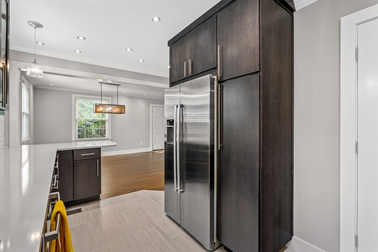 Kitchen with dark cabinetry, stainless refrigerator, white counters, and an adjoining dining area.