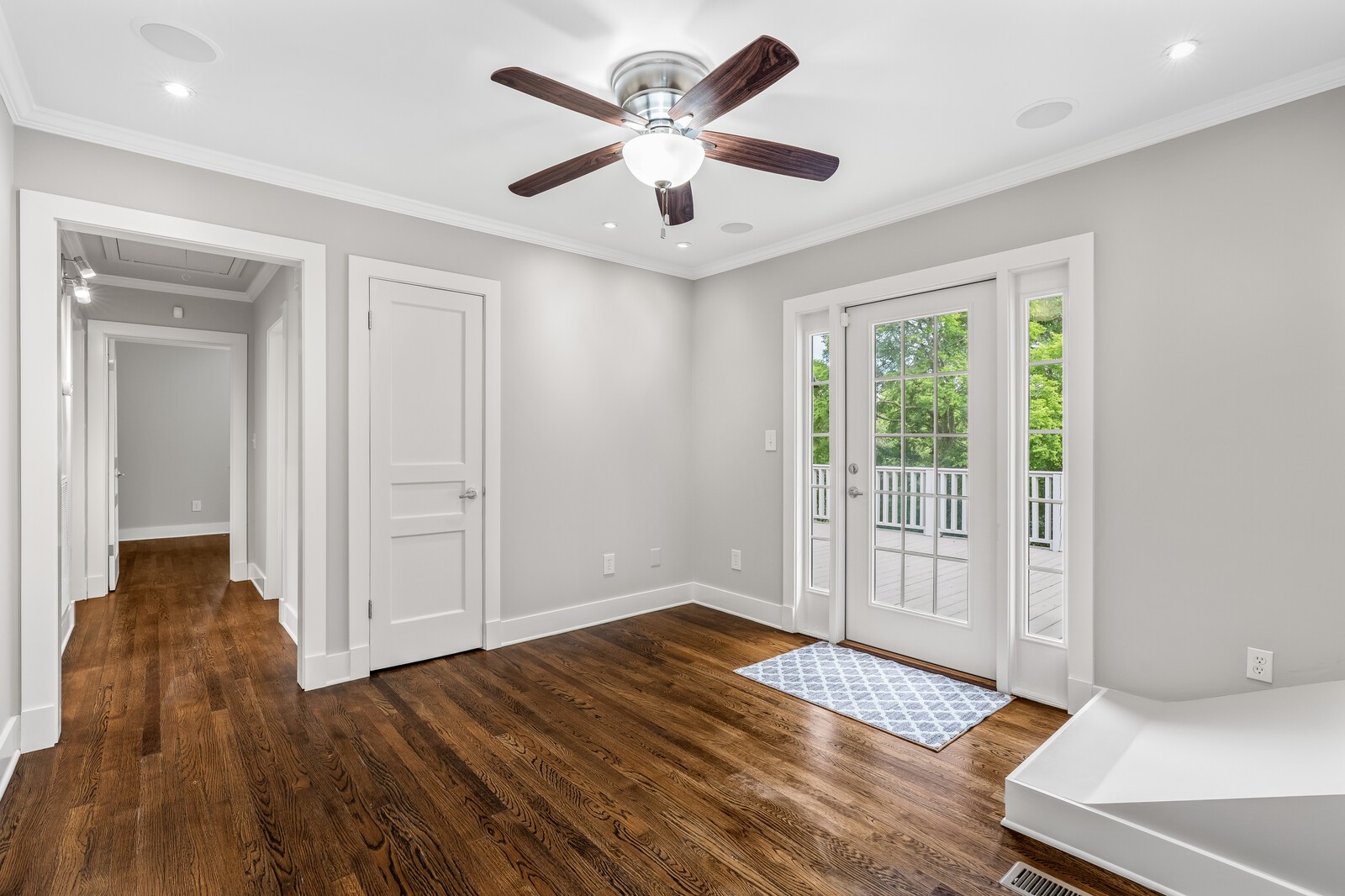 Empty bedroom with dark hardwood floors, ceiling fan, and glass doors opening to a deck.