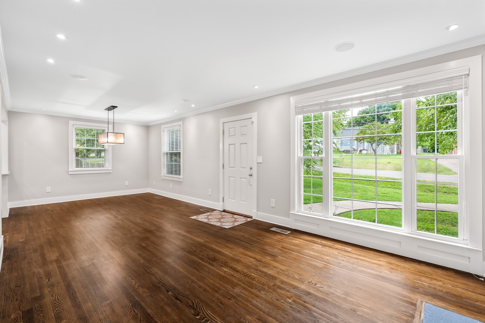 Vacant living room with dark hardwood floors and large windows overlooking a green lawn.