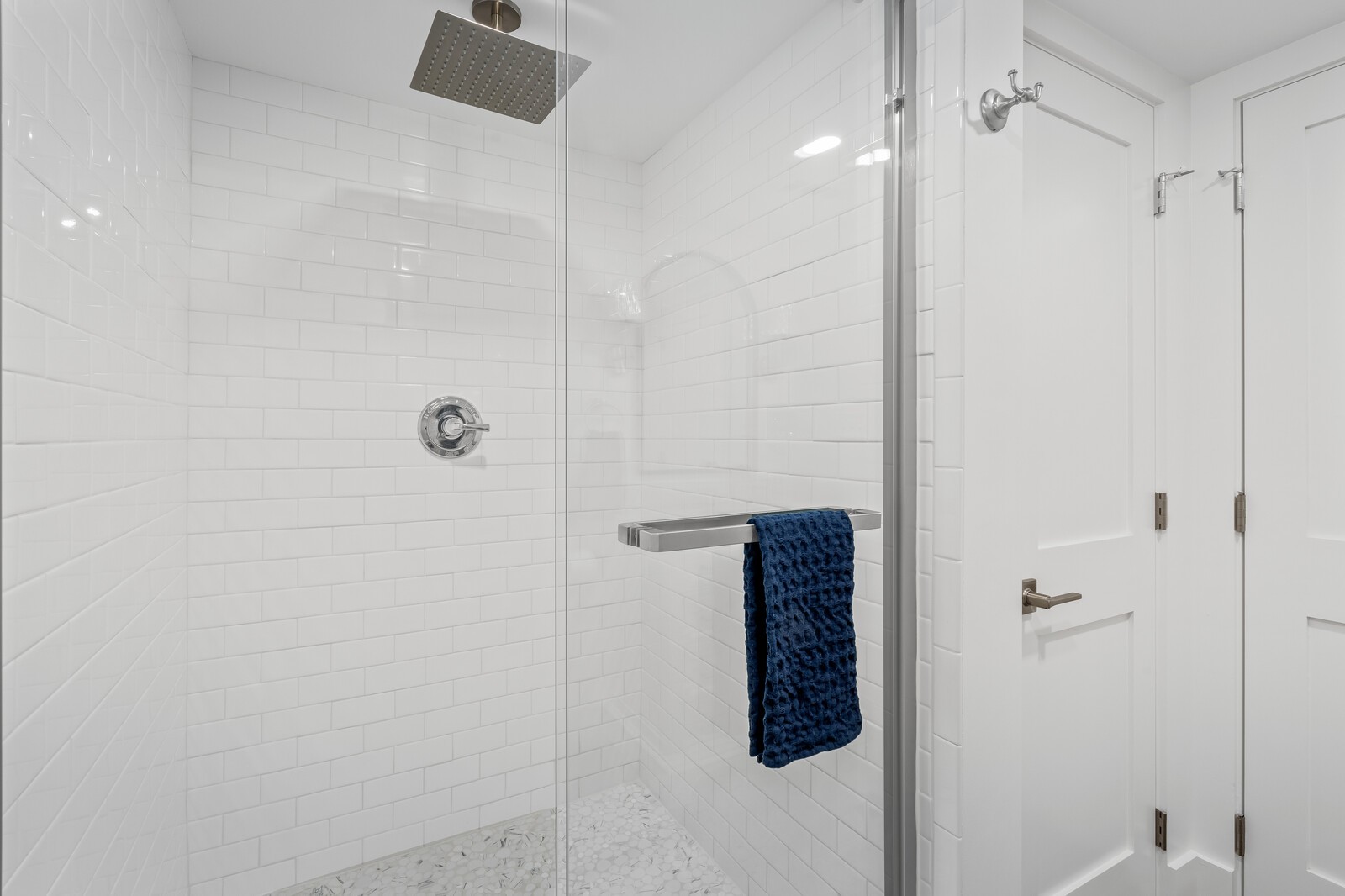 White subway tile shower with a square rainfall head, pebble floor, and navy towel.