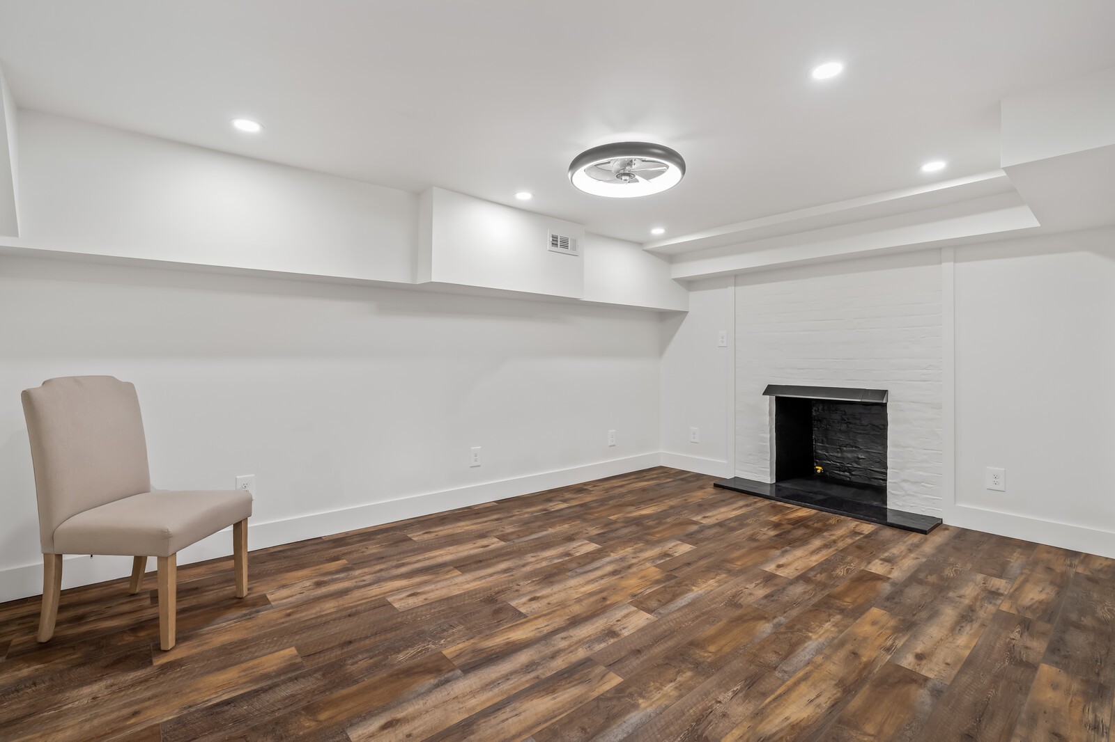 Bright room with a white brick fireplace, dark hearth, wood flooring, and a single chair.