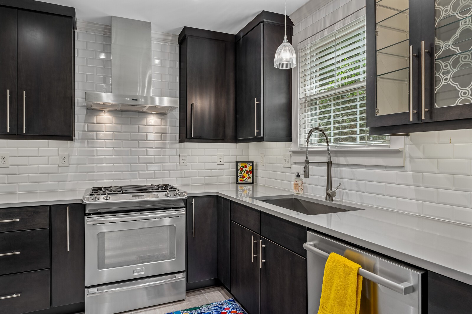 Kitchen with dark cabinets, white tile backsplash, stainless steel appliances, and a sink beneath a window.