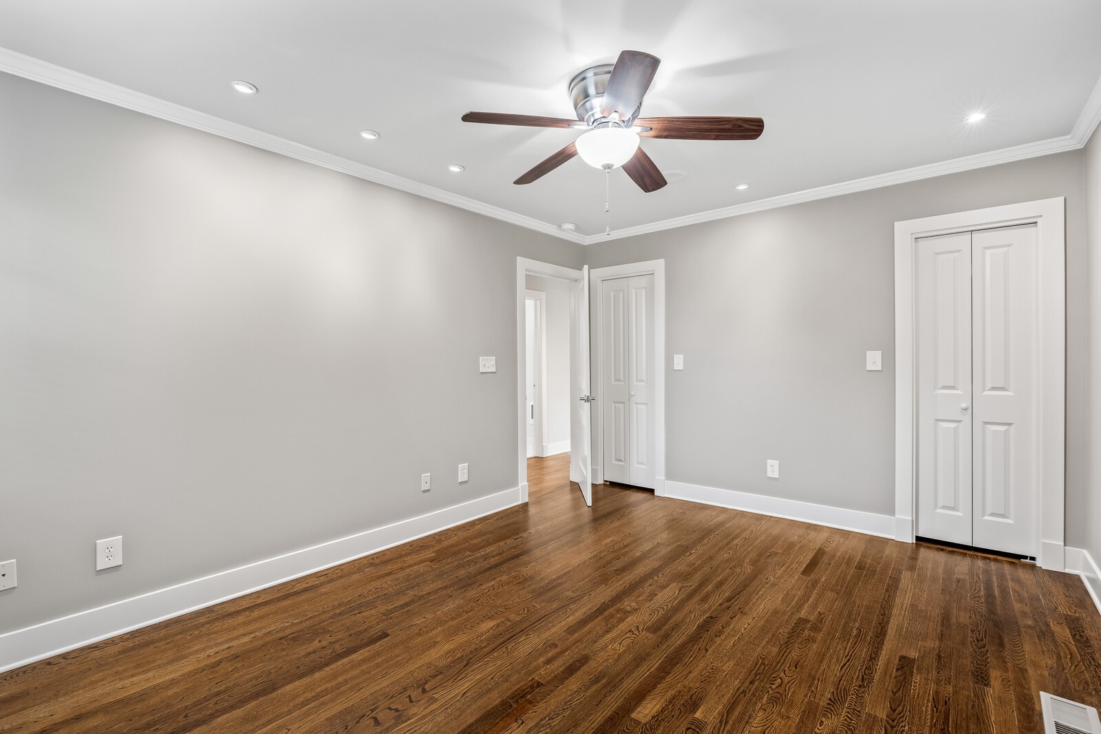 Vacant room with hardwood floors, gray walls, a ceiling fan, and a double-door closet.